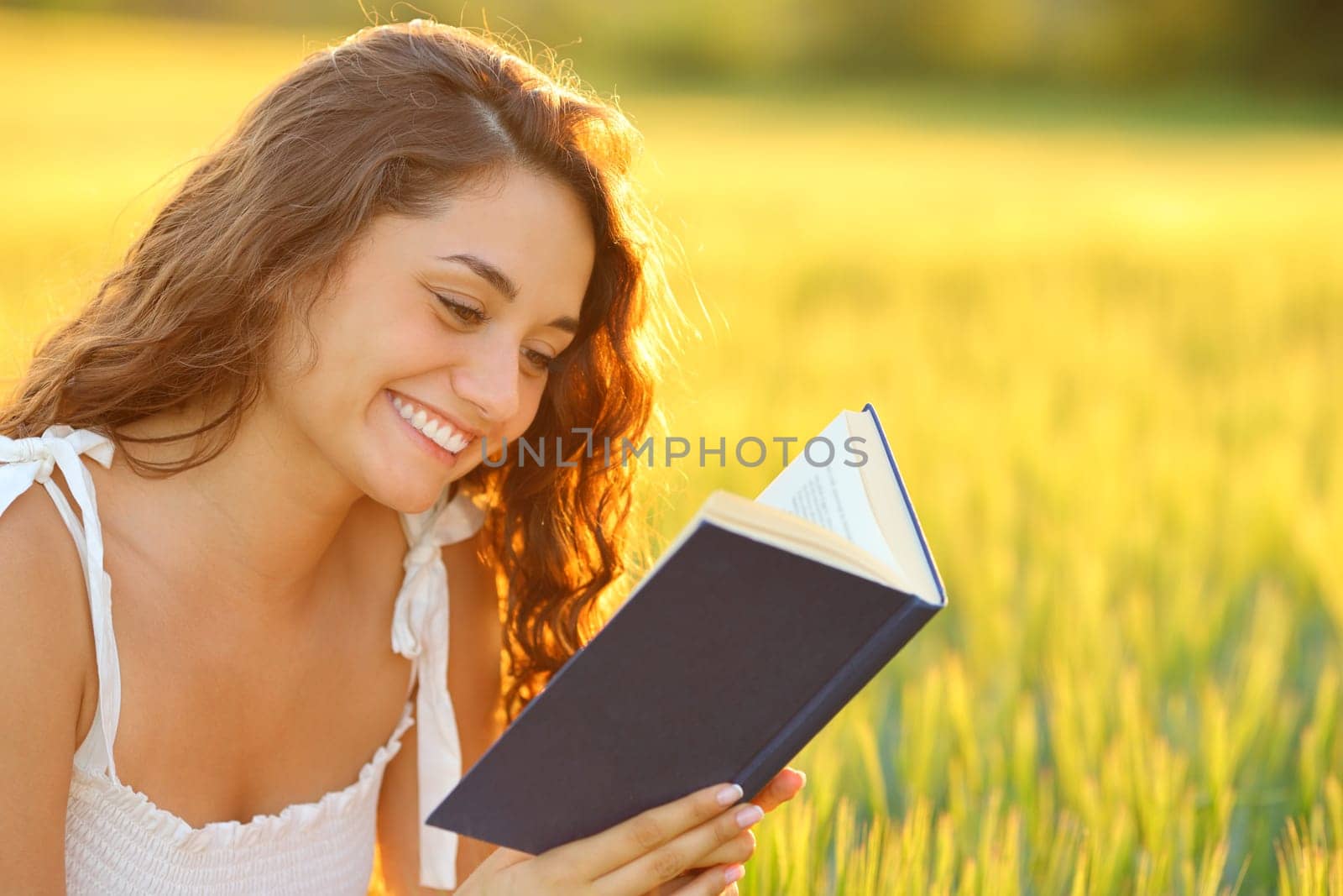 Happy woman reading a book smiling in a wheat field at sunset