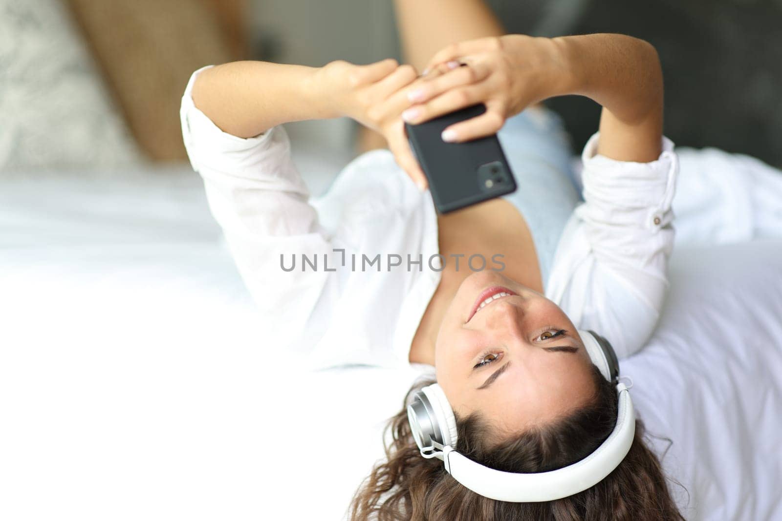 Happy woman listening to music wearing headphones on a bed