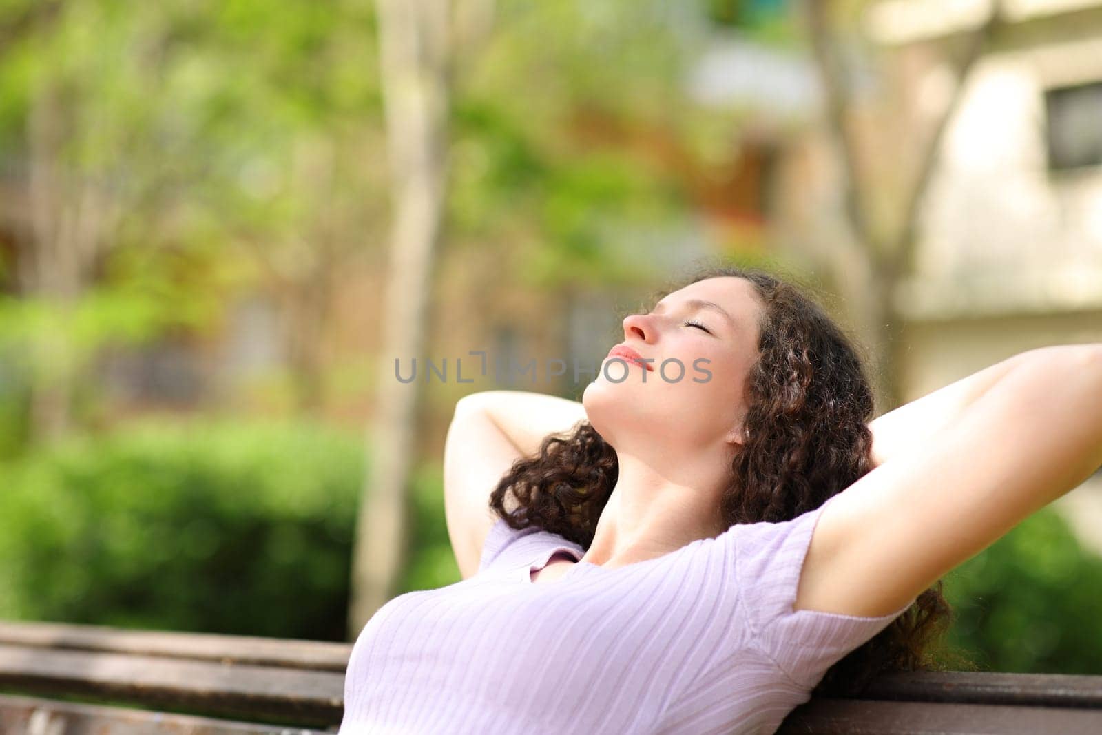 Relaxed woman resting with arms on head sitting in a bench in a park