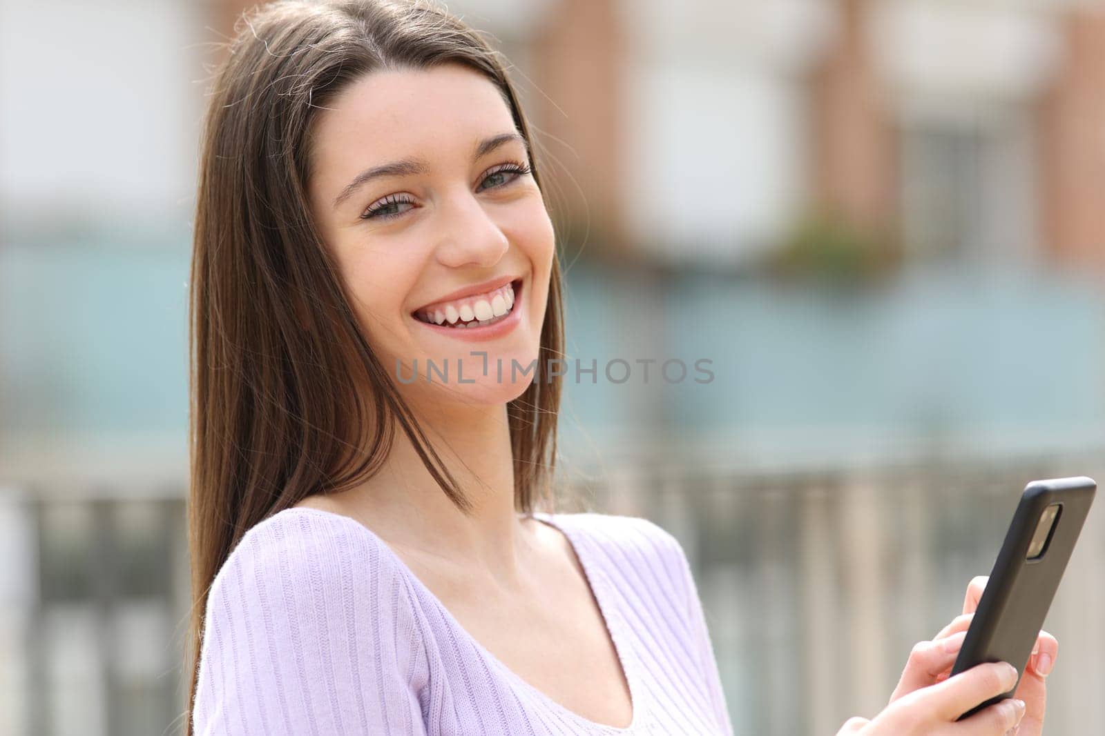 Portrait of a happy teen holding smart phone looking at camera in the street