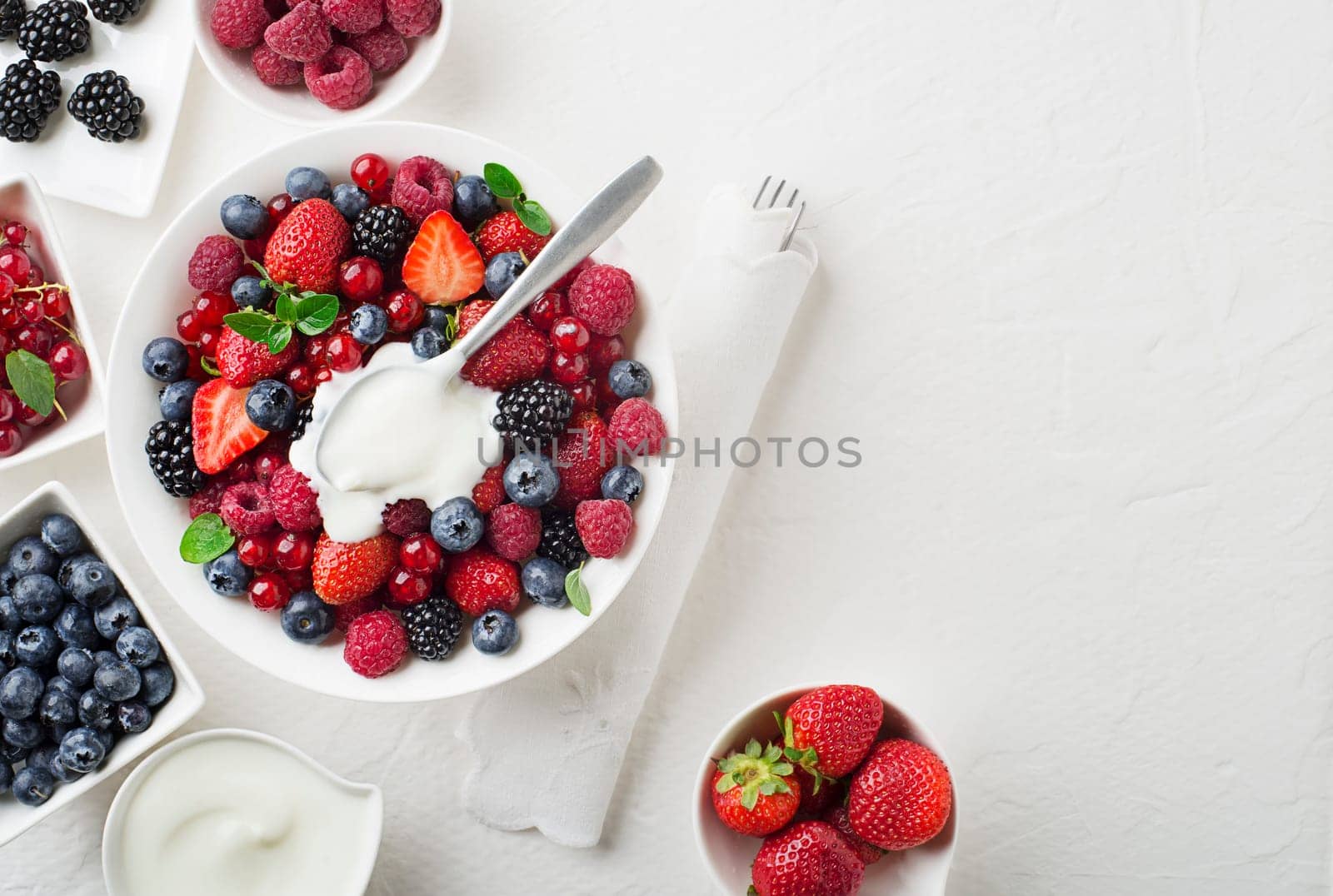 Bowl of healthy fresh berry fruit salad with cream on white background. Top view. Berries overhead closeup colorful assorted mix of strawberry, blueberry, raspberry, blackberry, red currant