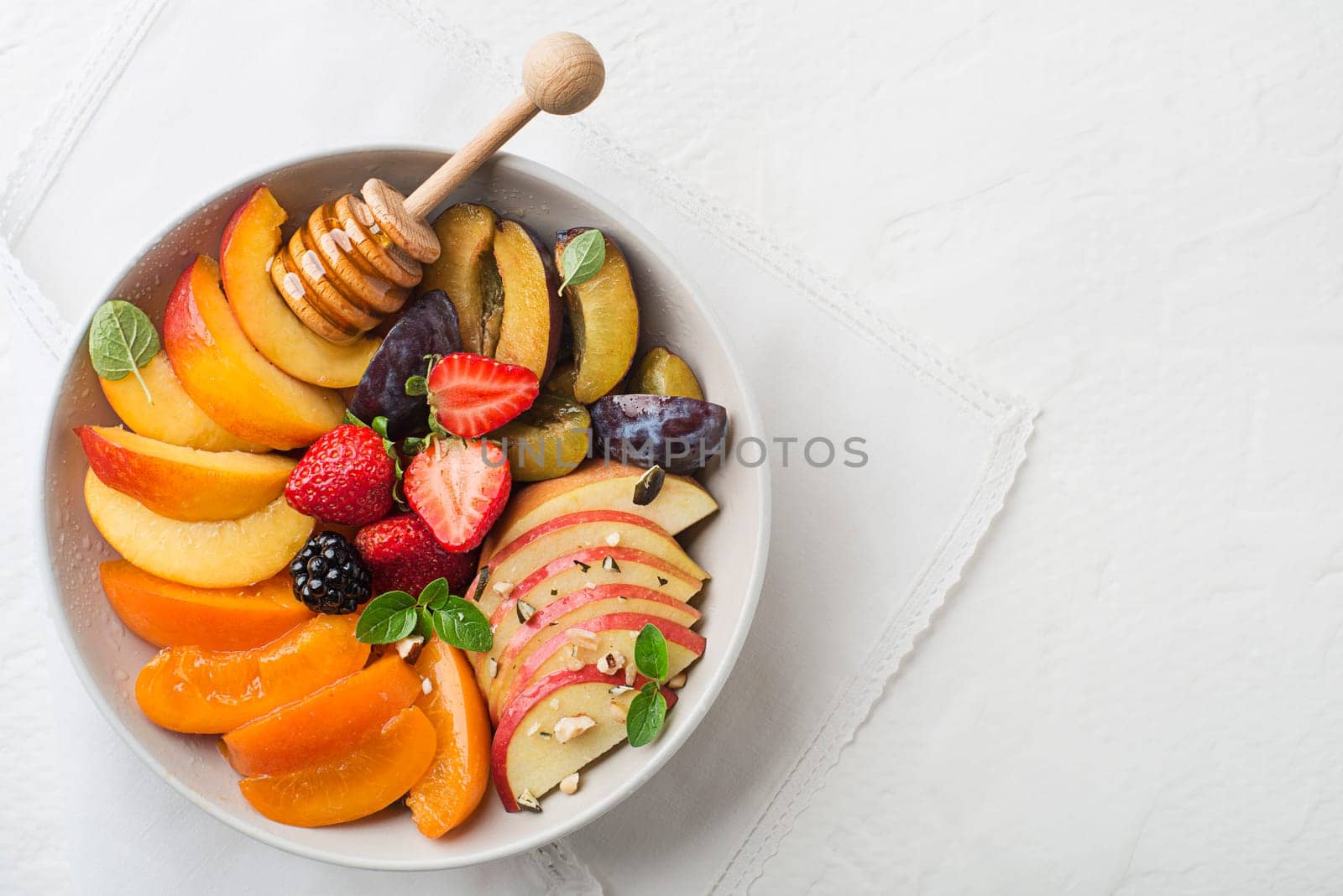 Bowl of healthy fresh fruit salad sweetened with honey on white background