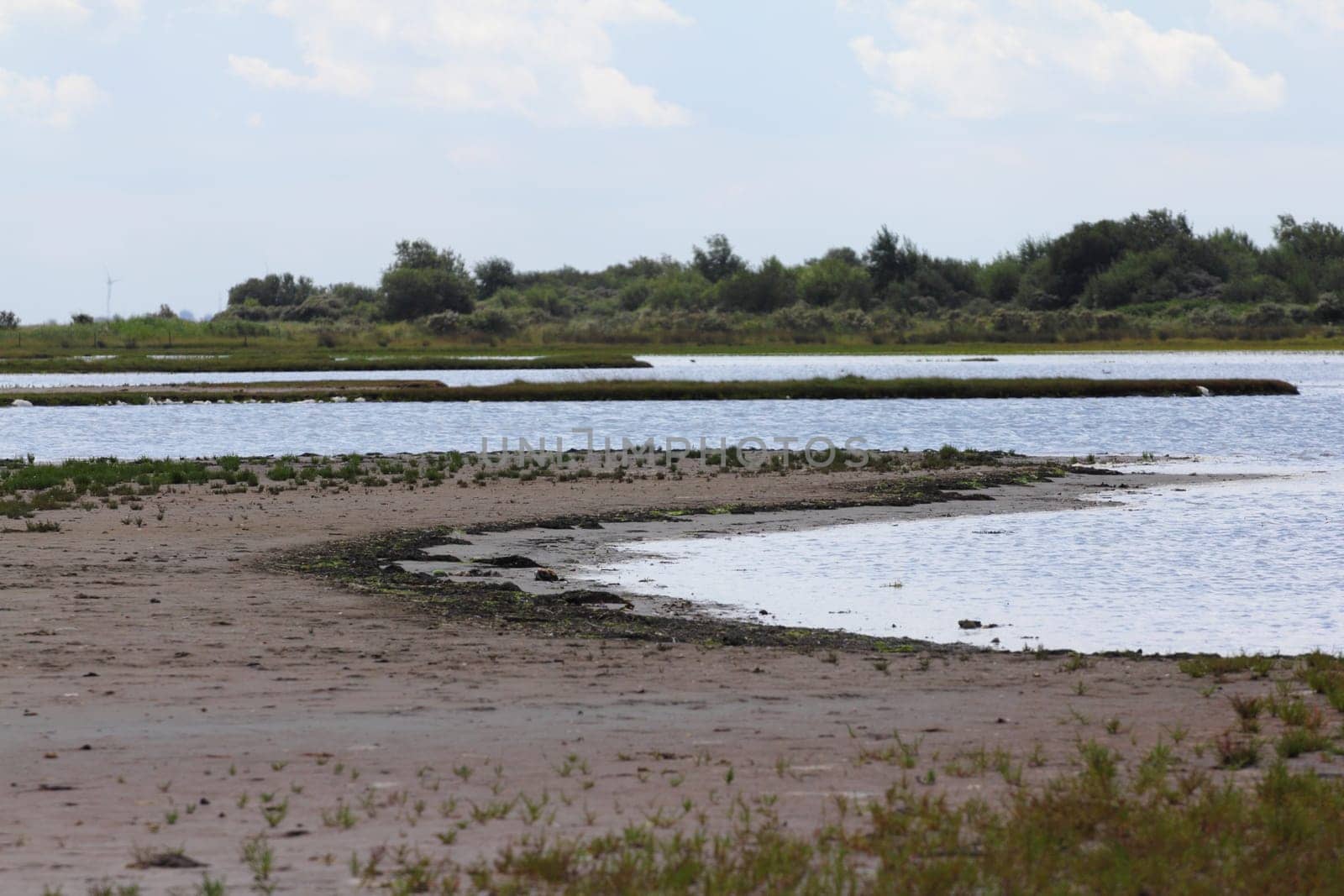 Water surface with small sand island, blue sky in background.Wasserfläche mit kleiner Sandinsel, blauer Himmel im Hintergrund.