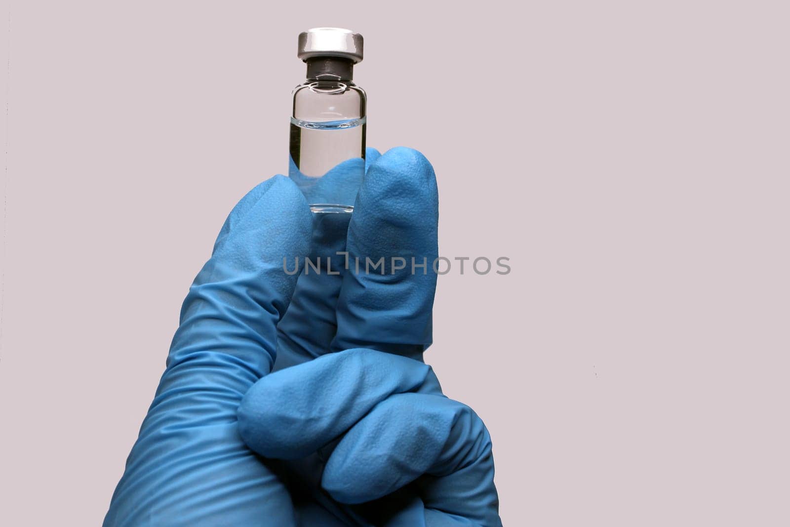 A hand in a blue medical glove close-up holding a vaccine against a light background. The concept of the fight against Covid19..