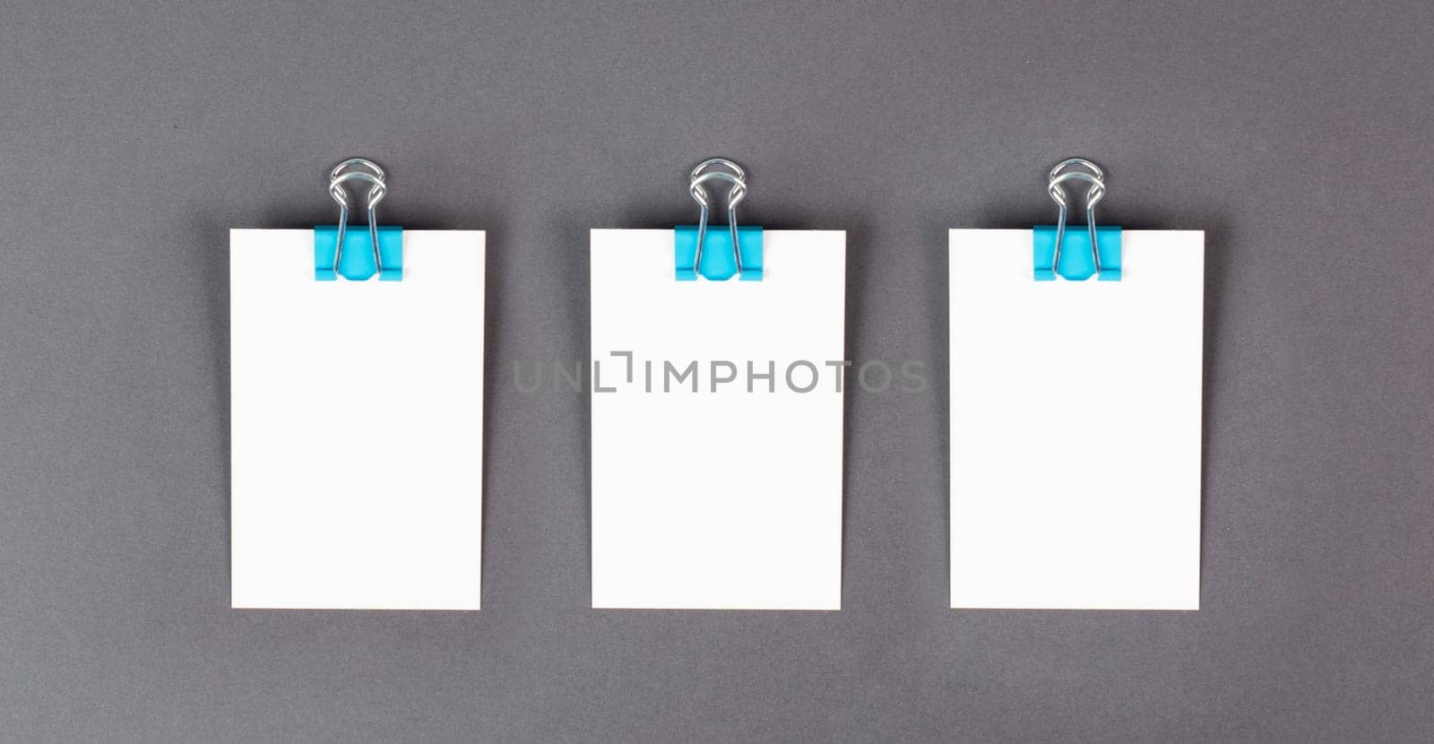 Blank white paper with a paperclip on a gray colored background, copy space for text, reminder or message in the office, communication concept