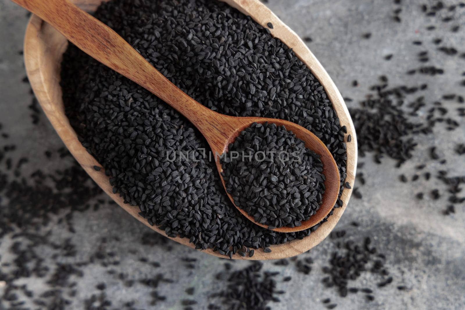 Indian spice Black cumin (nigella sativa or kalonji) seeds in bowl with spoon on grey table top view. Traditional medicine, healthy and vegetarian food concept.