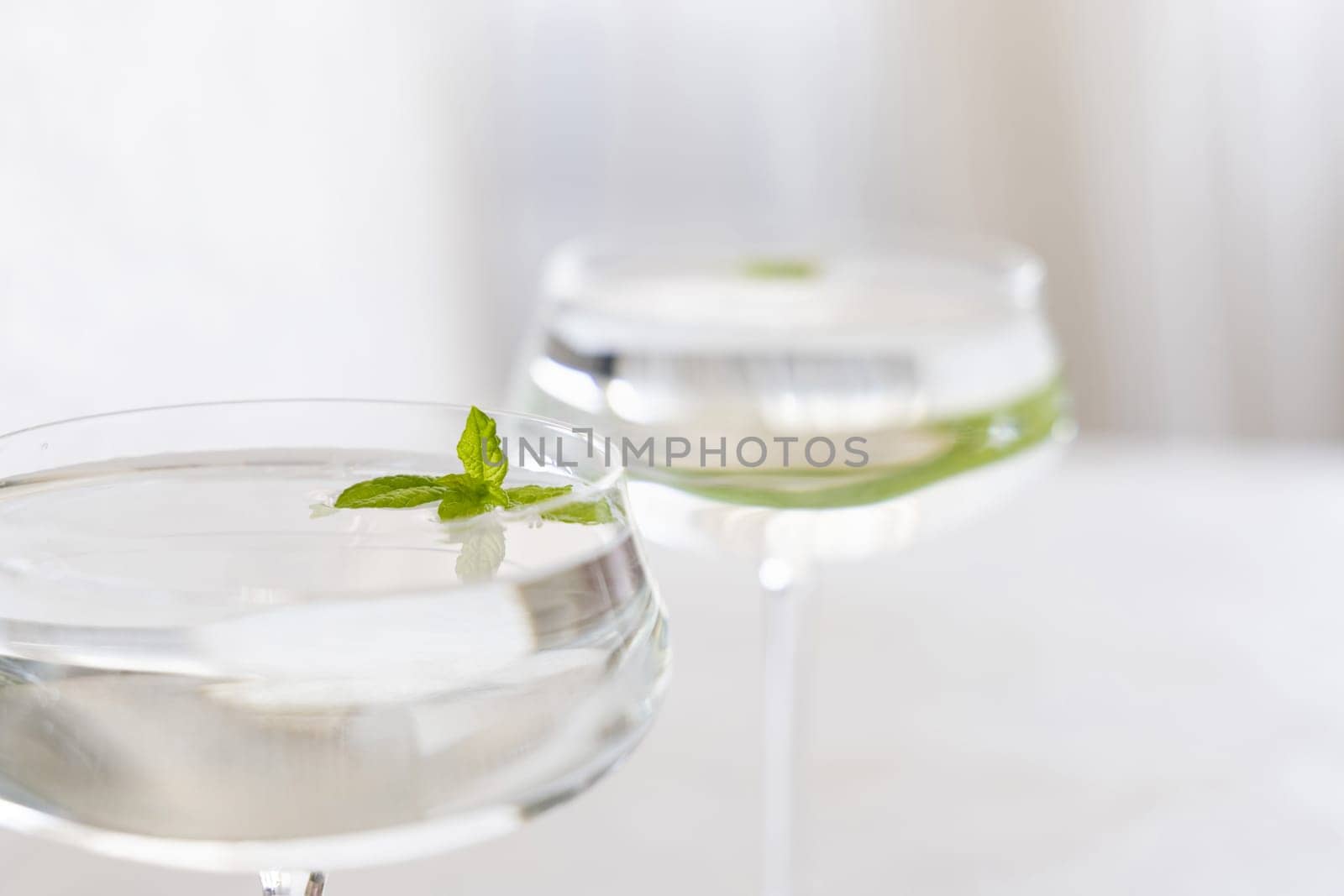 Transparent cocktail with ice cubes in a glass decorated with mint leaves close up. Tropical drink at the bar. Summer vacation mood. Analcolic mocktail drink