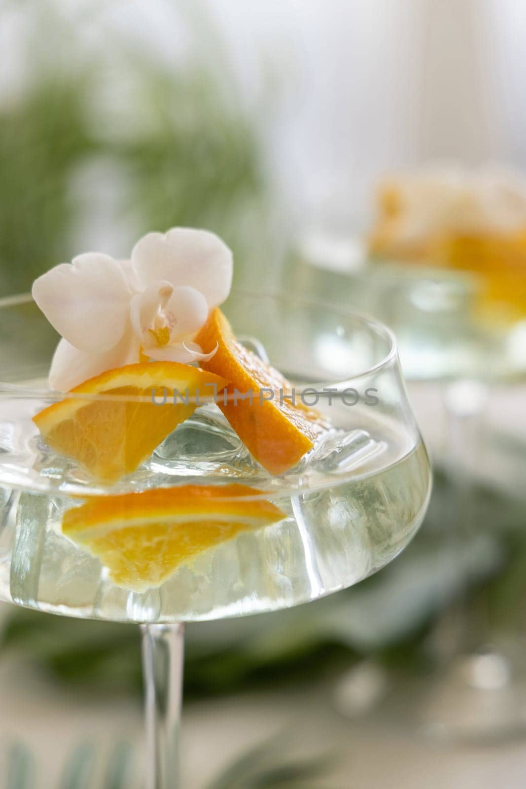 Exotic Cocktail with ice cubes in a coupe glass decorated with slices of orange and orchid flower close up. Tropical drink at the bar outdoor. Summer vacation mood