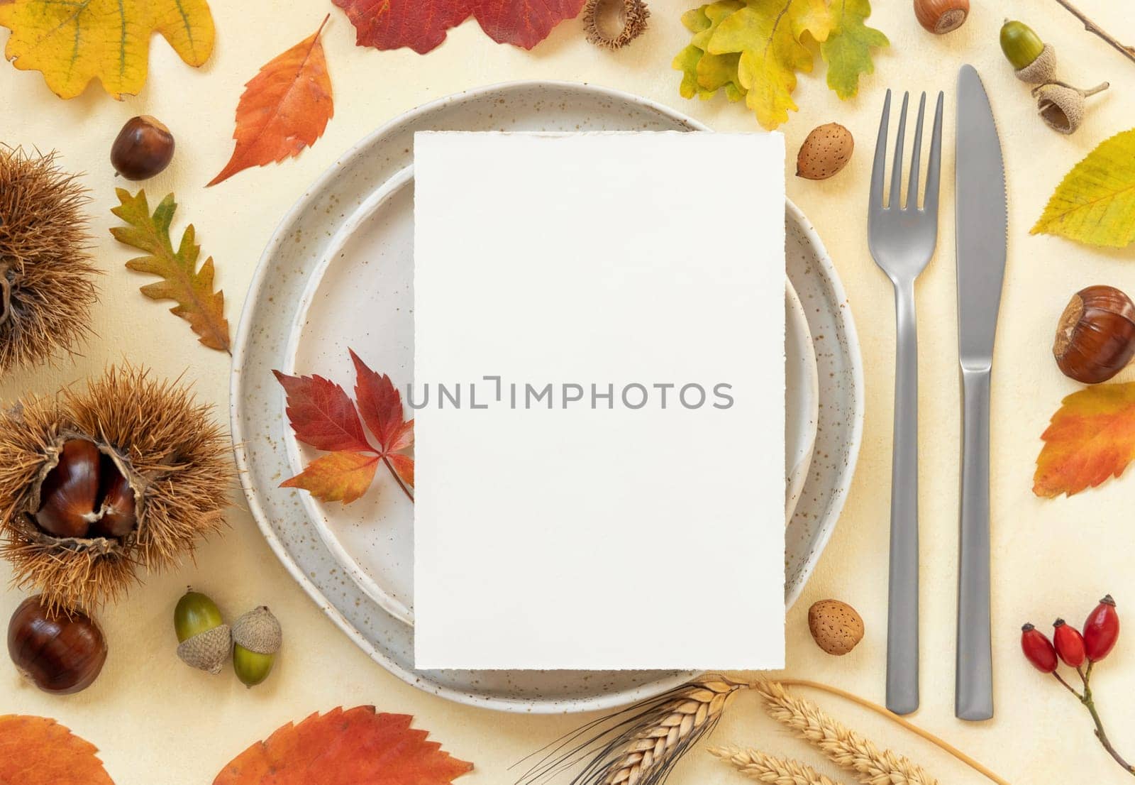 Autumn table place with colorful leaves and blank card top view. Mockup of fall vertical card on light yellowtable, flat lay, copy space. Harvest, Halloween and Thanksgiving season