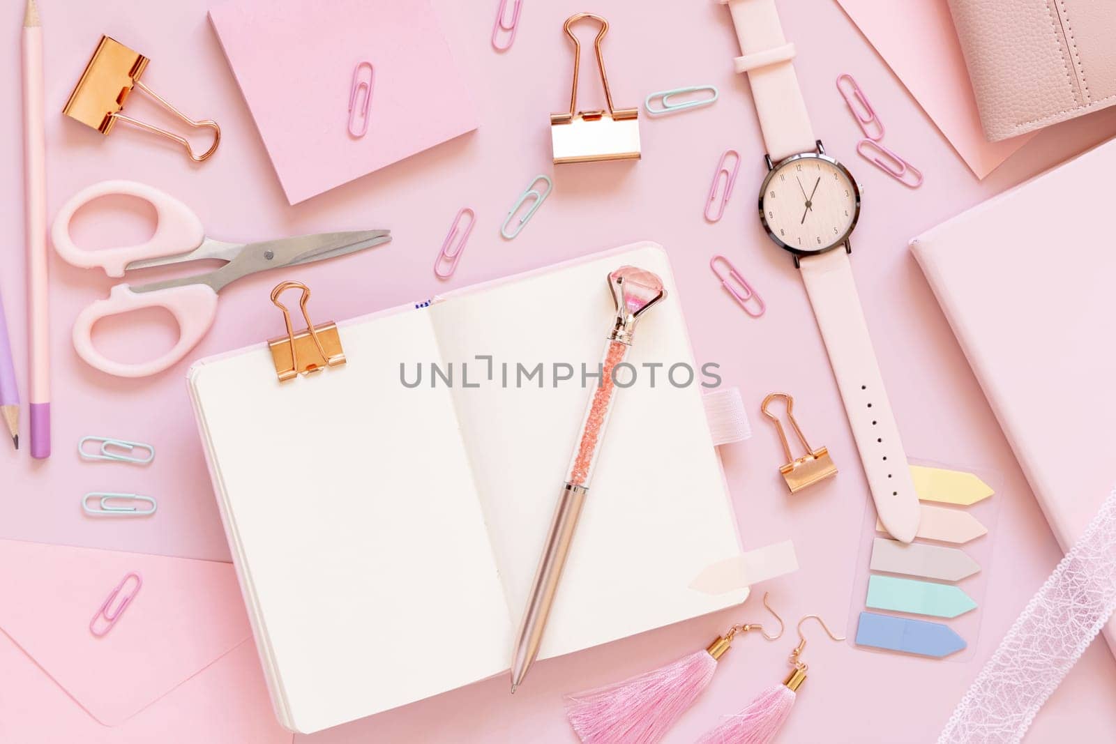 Opened notebook and Pink school accessories on pastel pink, Top view, textbook mockup. Girly workplace with scissors, pencils, pen, paperclips, earrings and watch. Back to school concept