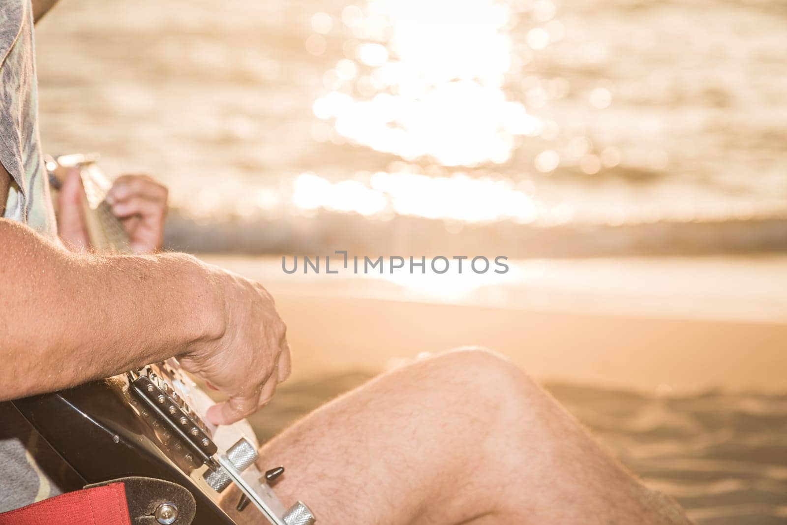 Romantic young man sitting on the sand at sunset with playing the guitar