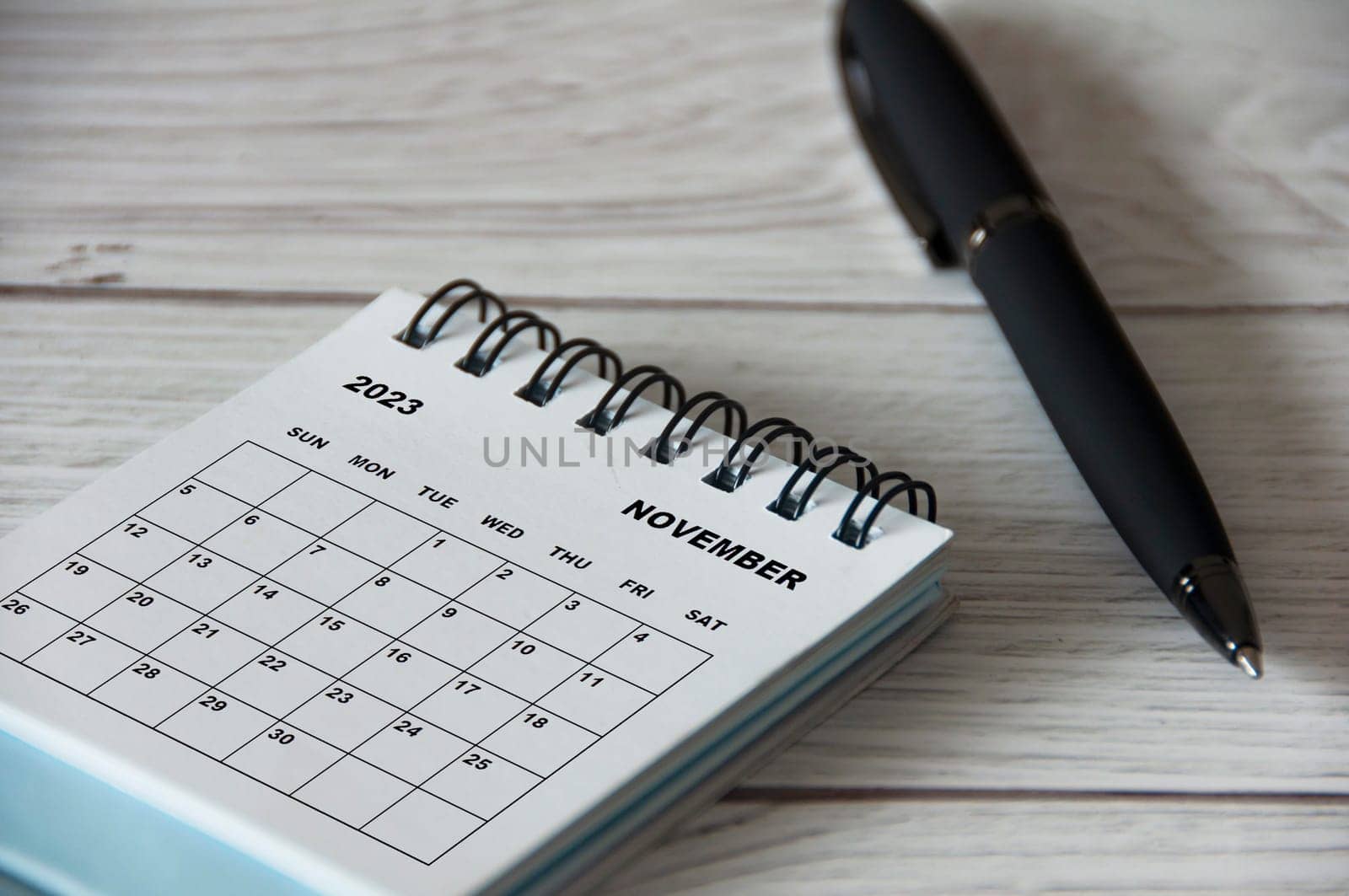 November 2023 white desk calendar with black pen on wooden table. Calendar concept