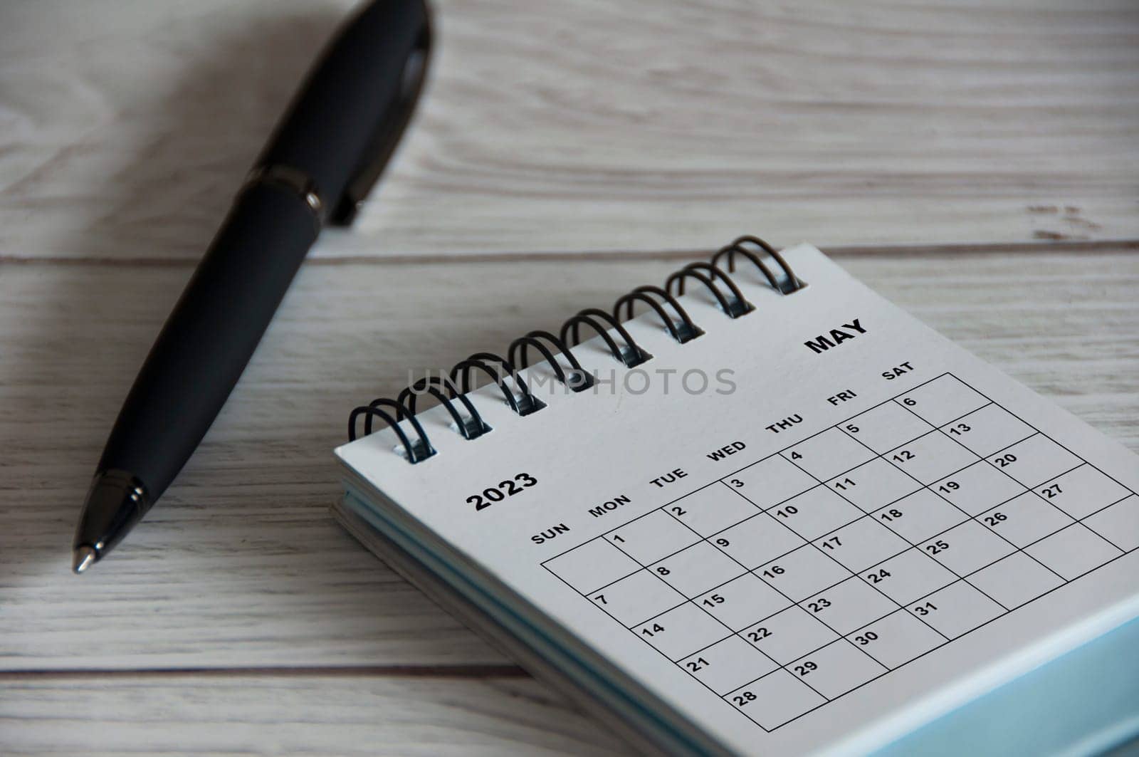 May 2023 white desk calendar with black pen on wooden table. Calendar concept