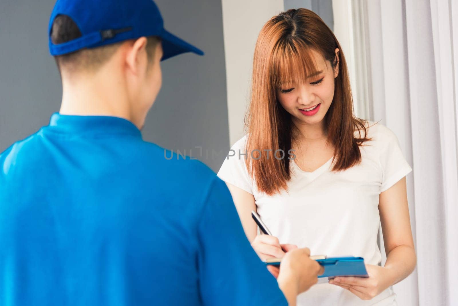 Asian beautiful customer young woman signing delivery in clipboard get her package from service courier man, smiling female signature receipt of delivery package at door front house