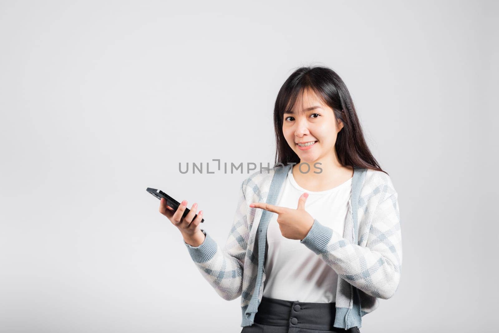 Woman excited celebrating win yes, great news on smartphone she pointing finger to mobile phone studio shot isolated white background, young female smiling having success after received promotion