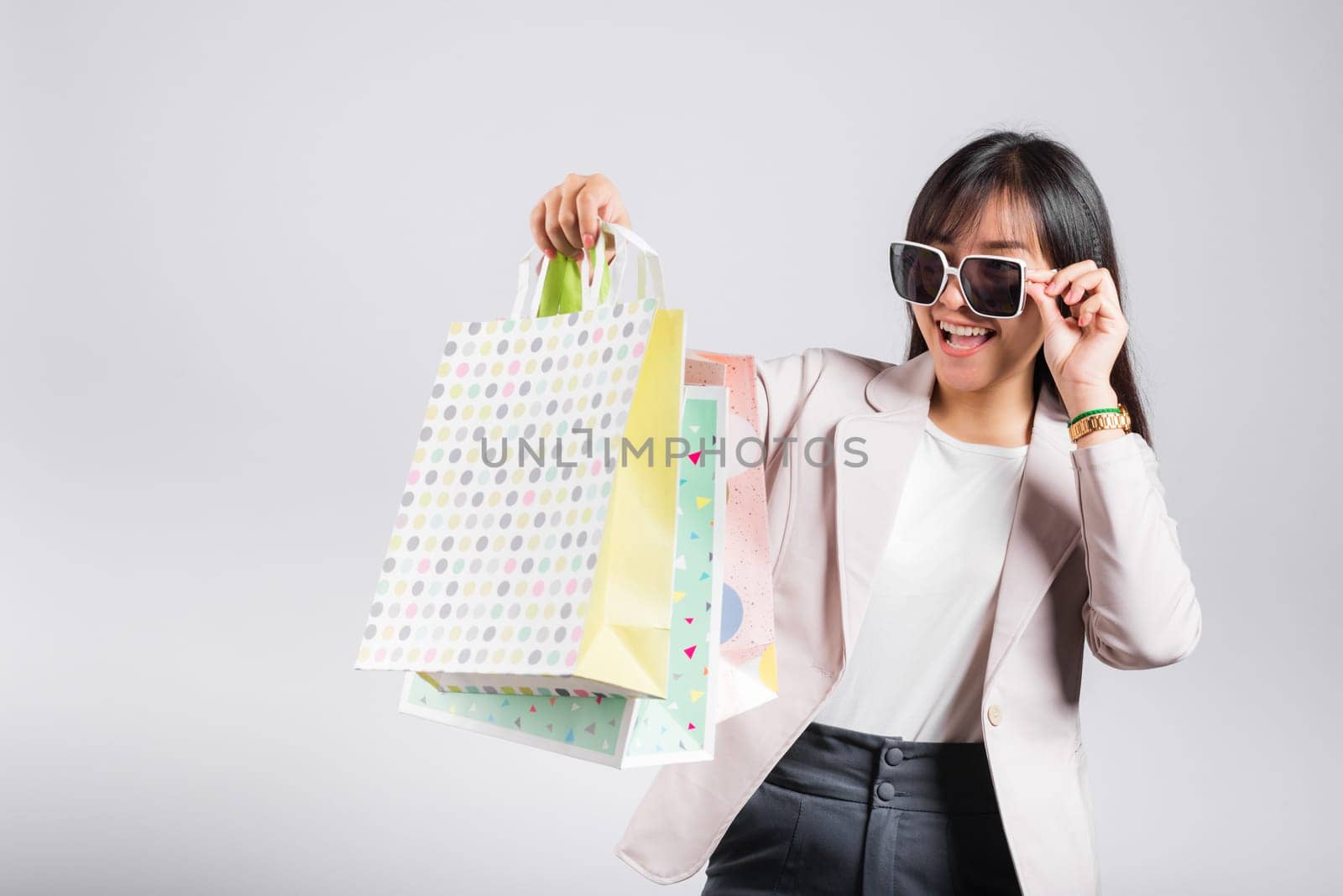 Happy woman with glasses confident shopper smiling holding online shopping bags colorful multicolor, Portrait excited Asian young female purchase studio shot isolated on white background, fashion sale