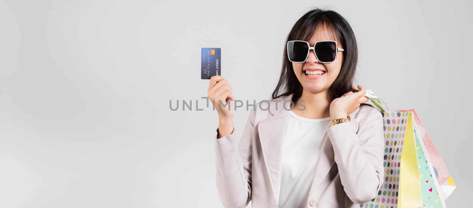 Woman with glasses confident shopper smile hold online shopping bags and credit card for payment on hand, Portrait excited happy Asian female fashion shop studio shot isolated on white background