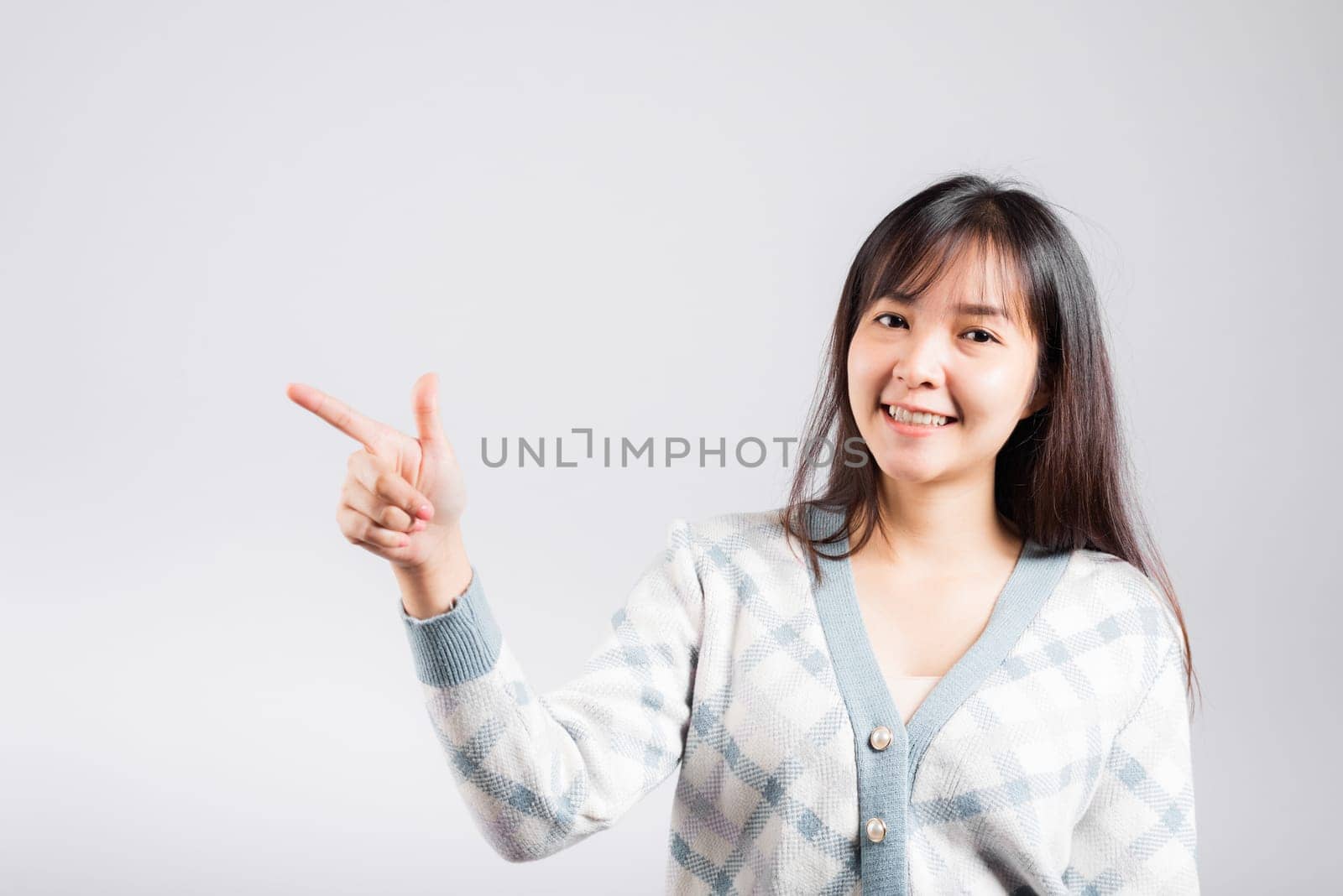 Smiling happy woman pointing finger out space, Portrait Asian beautiful young female point into empty looking to side away, studio shot isolated on white background with copy space