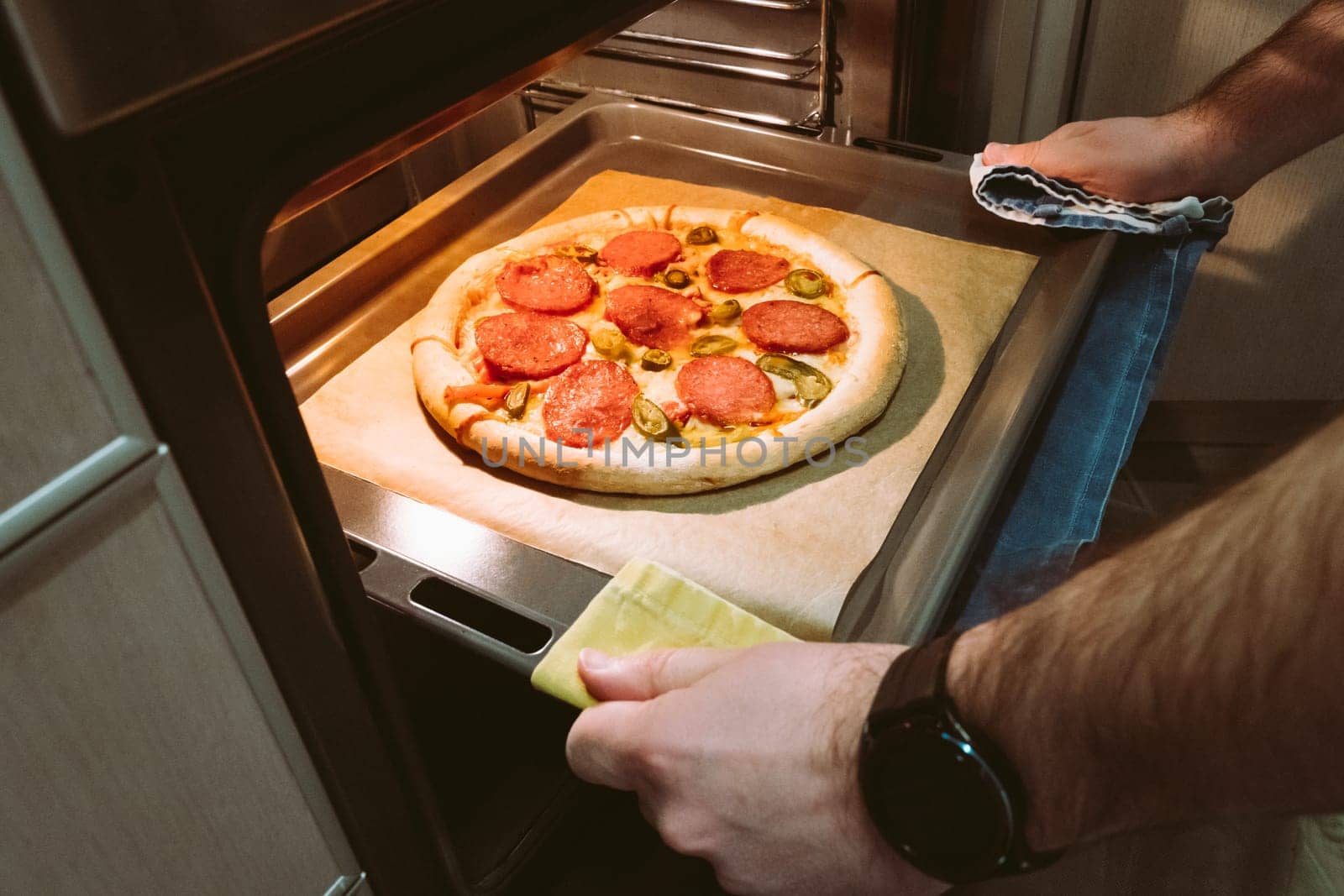 A man pulls a tray of pepperoni pizza from the oven at home.