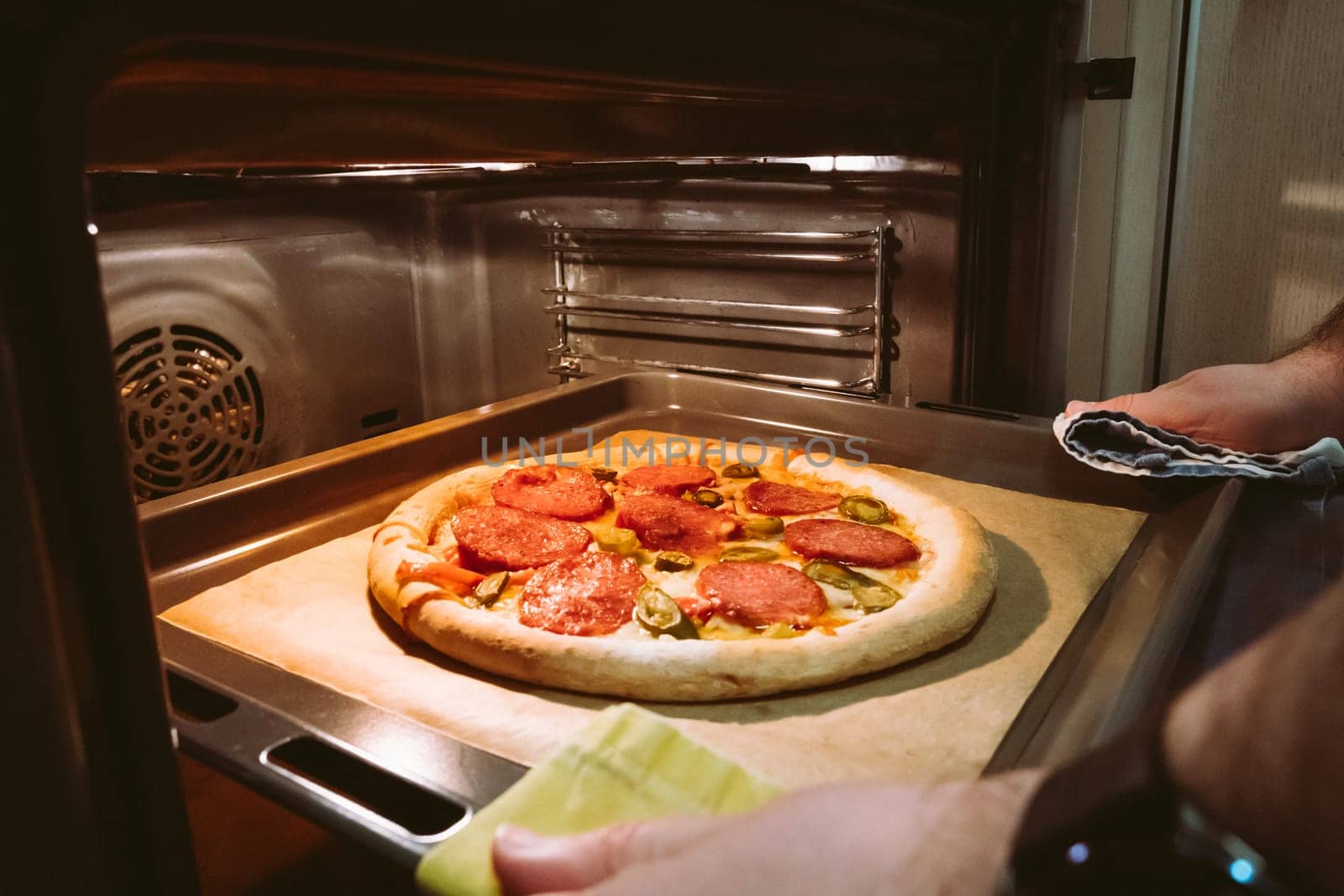 A man's hands pull out a homemade pepperoni pizza from the oven.
