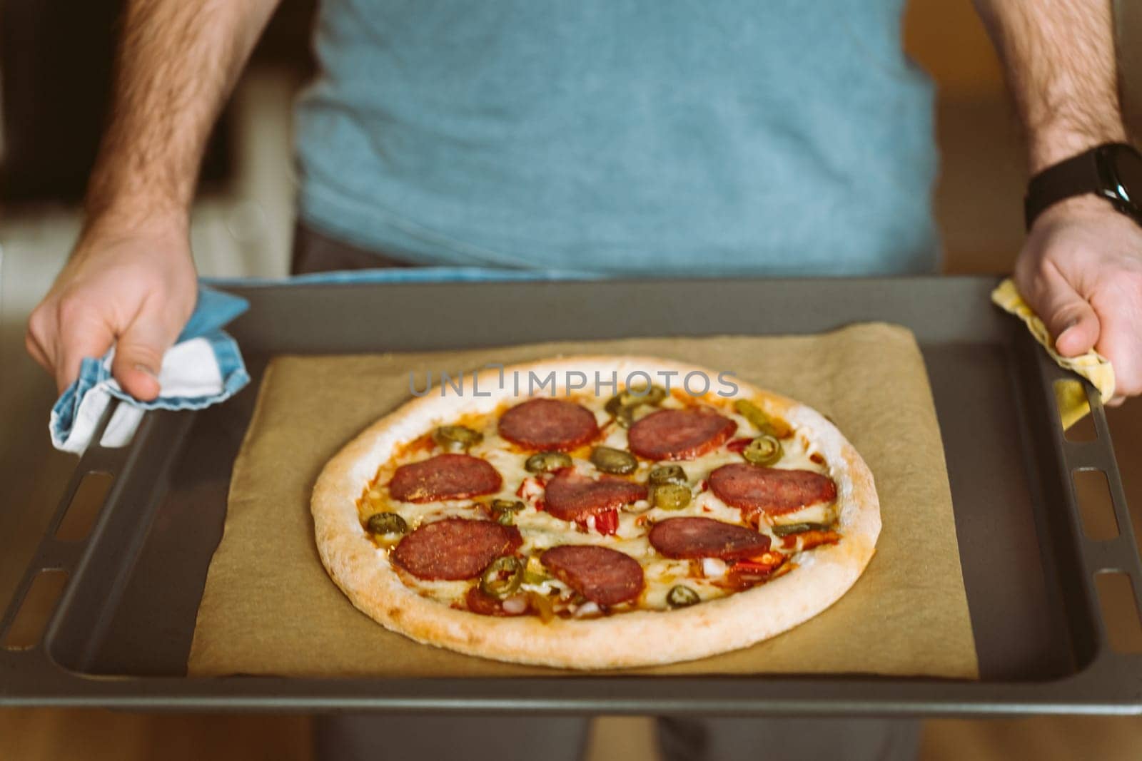 A man holds a baking sheet with pizza. Baking sheet covered with baking paper.