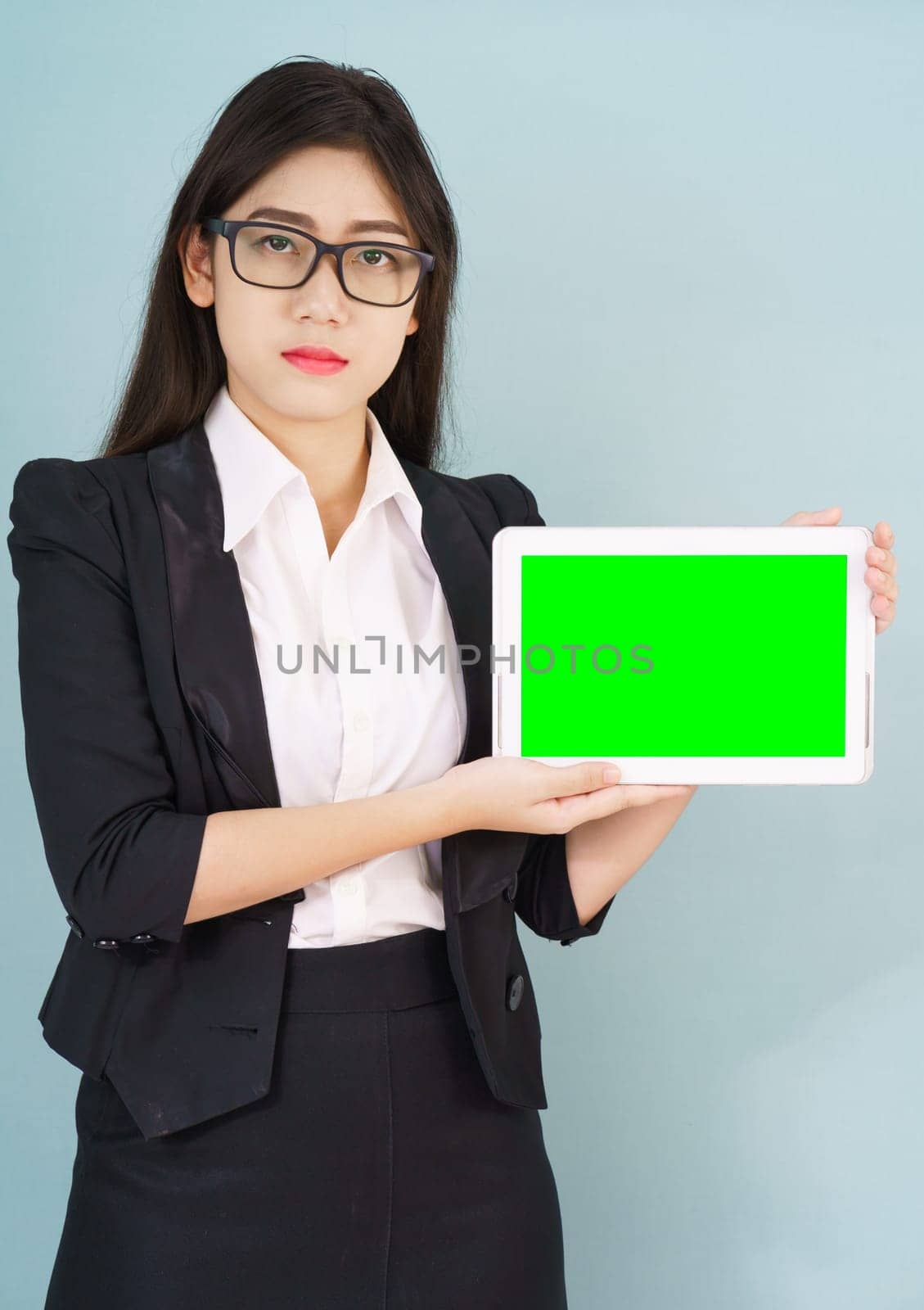 Young asian women in suit holding her digital tablet mock up standing against green background