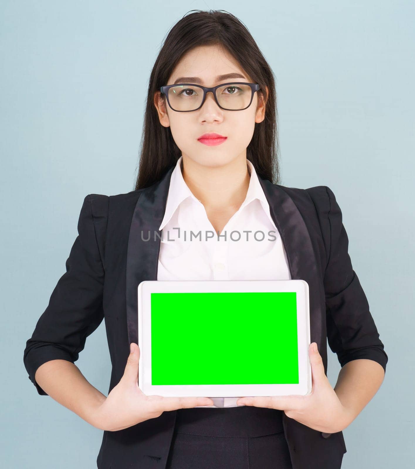 Young asian women in suit holding her digital tablet mock up standing against green background