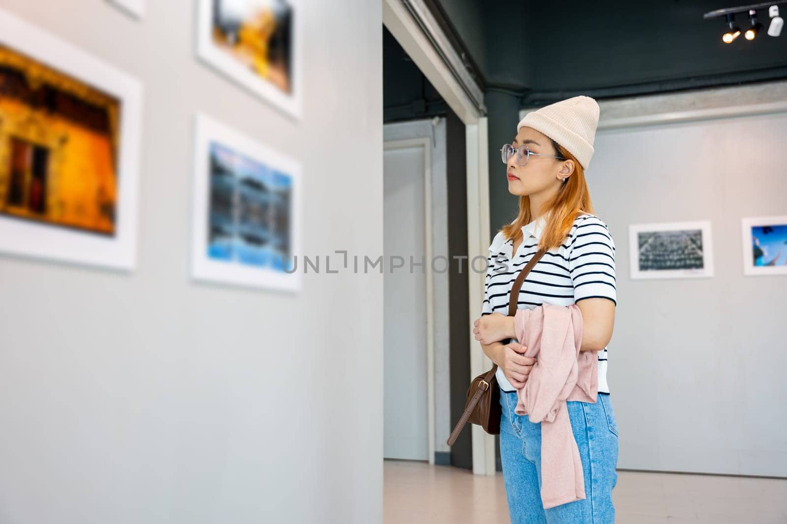 Woman standing she looking art gallery collection in front framed paintings pictures on white wall, Asian people watch at photo frame to leaning against at show exhibition artwork gallery, Side view