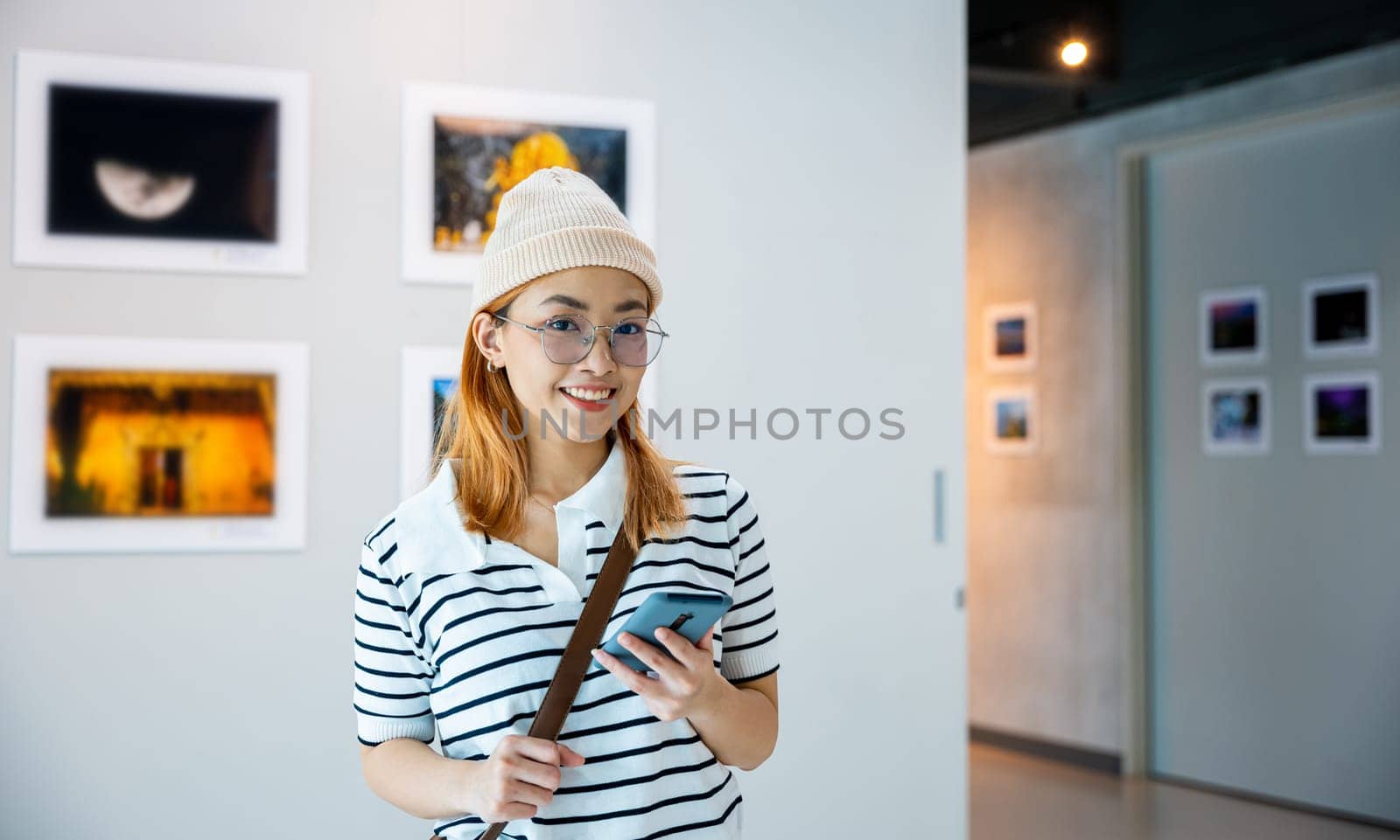 Visitor woman standing takes picture art gallery collection in front framed paintings pictures with mobile phone, Asian female watching at photo frame with smartphone at artwork gallery show