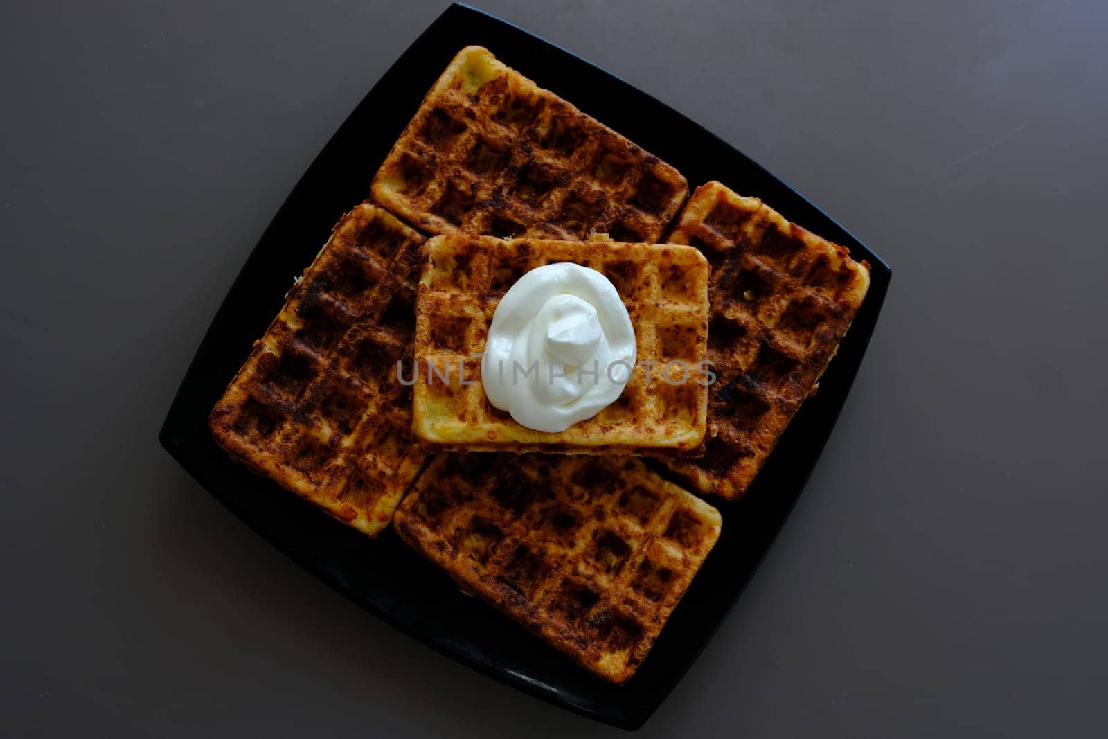 Belgian waffles on a black plate, on the biege table and souse it in sour cream