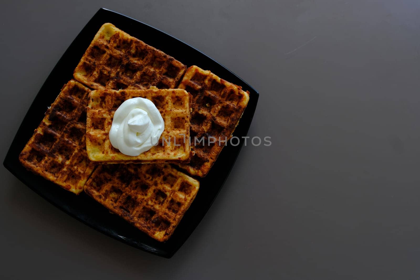 Belgian waffles on a black plate, on the biege table and souse it in sour cream