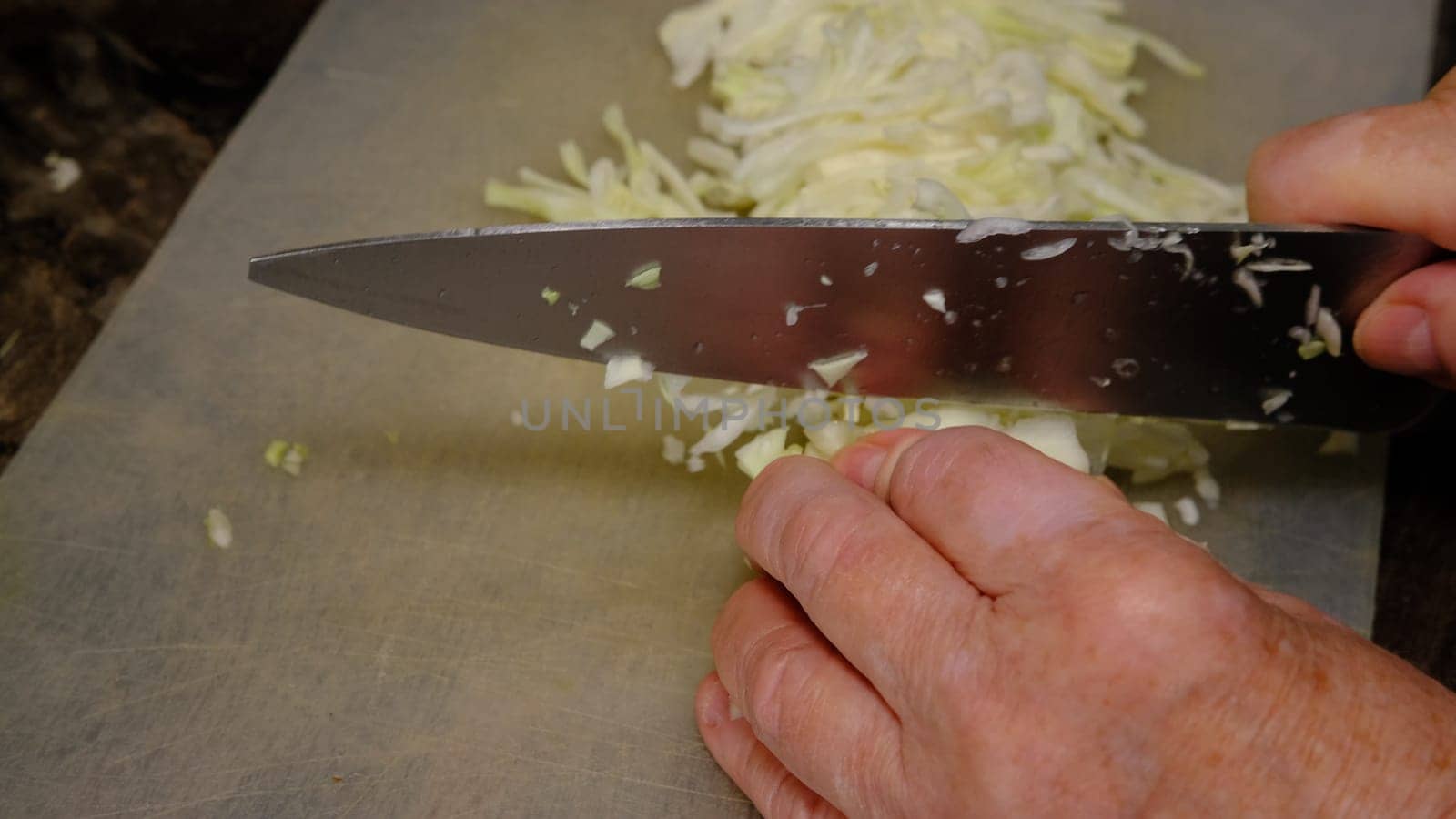 old women's hands with a knife cut cabbage on the cutting Board.