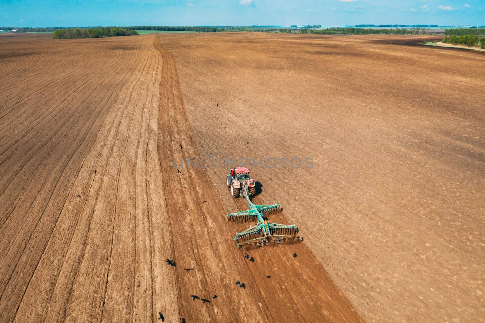 Aerial View. Tractor Plowing Field In Spring Season. Beginning Of Agricultural Spring Season. Cultivator Pulled By A Tractor In Countryside Rural Field Landscape.