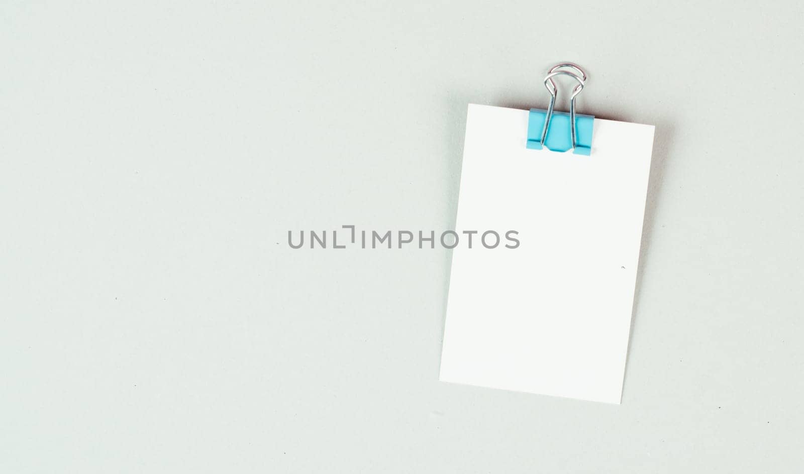 Blank white paper with a paperclip on a gray colored background, copy space for text, reminder or message in the office, communication concept
