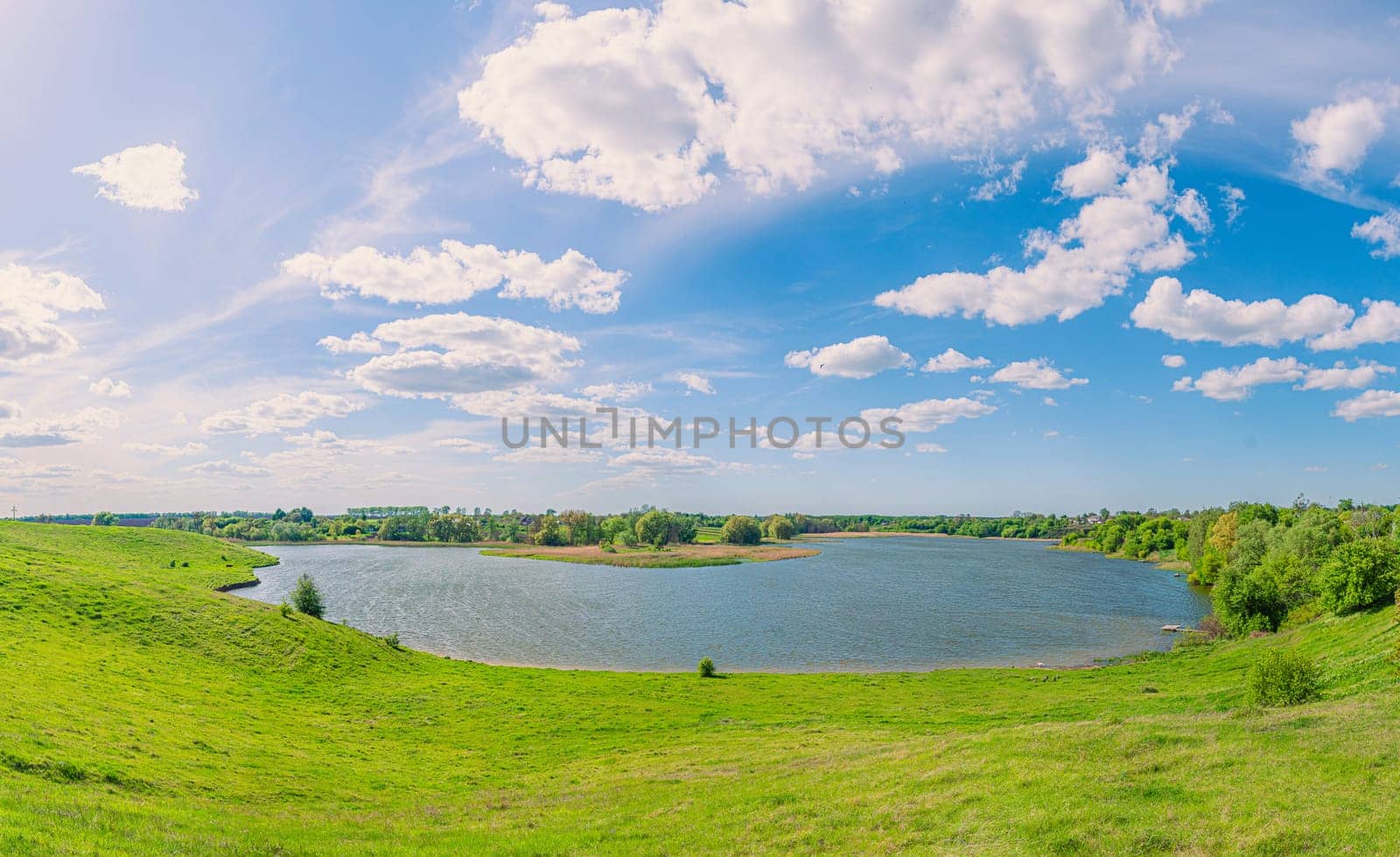 A beautiful lake in the middle of green hills under a blue sky with clouds in the village of Vchorayshe, Zhytomyr Region, Ukraine