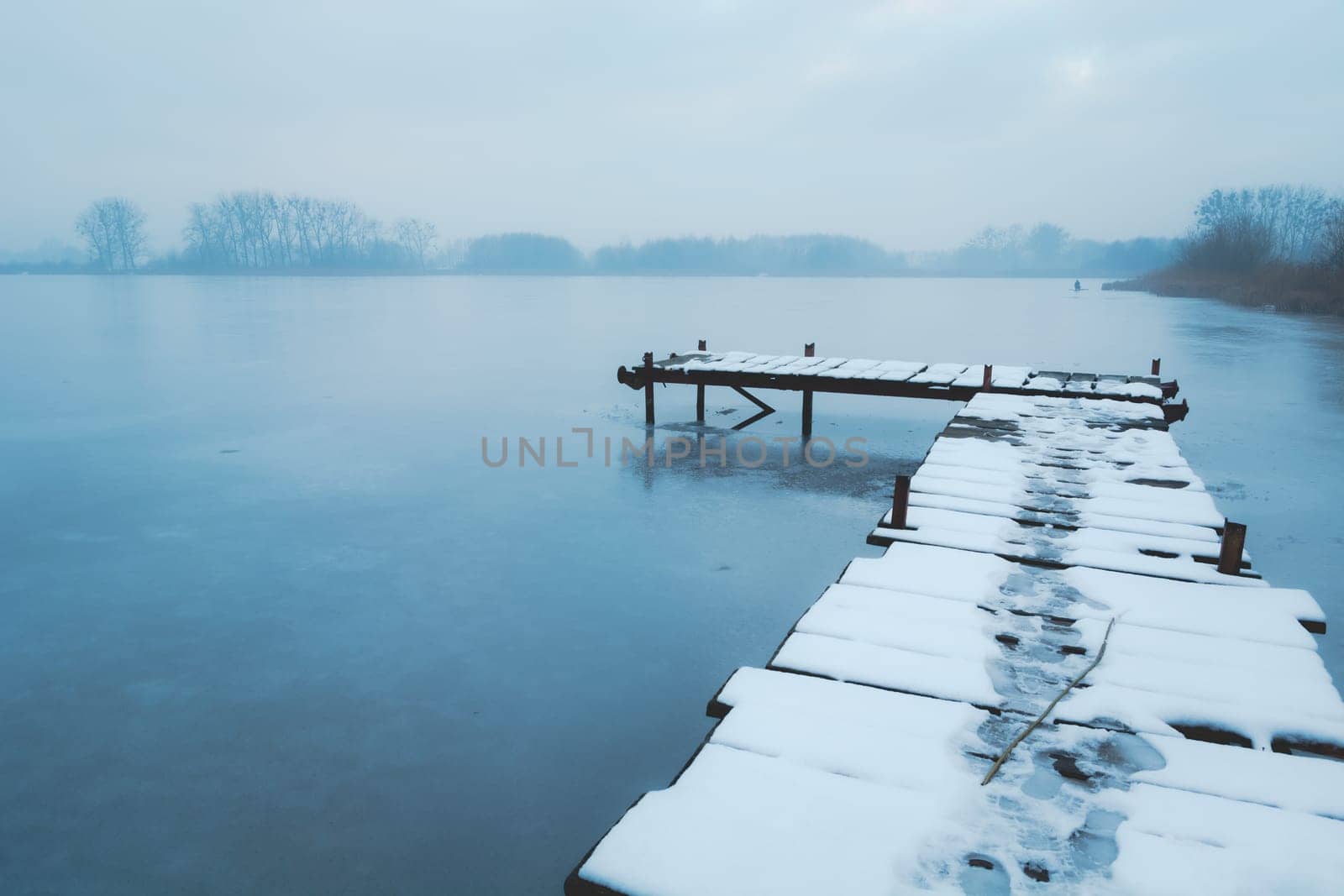 A snow-covered wooden pier on a frozen lake, December day