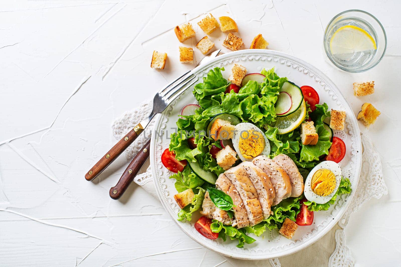 Fresh green salad with chicken breast, crouton and boiled egg on white table background