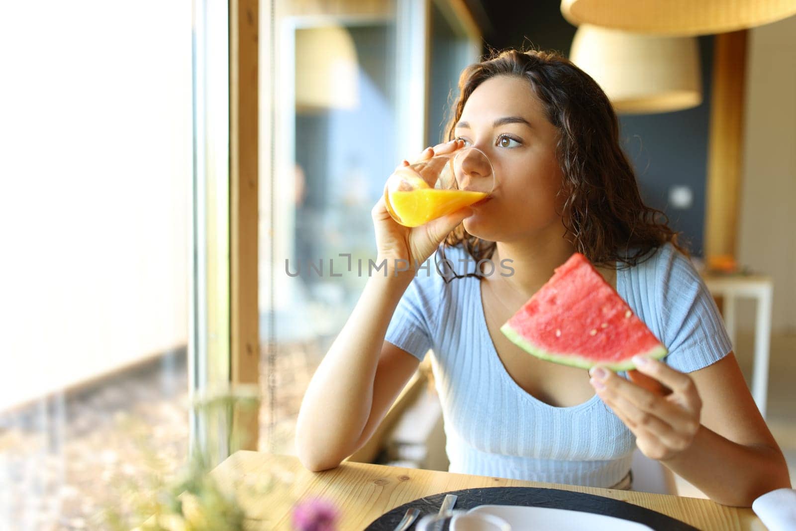 Woman drinking orange juice and eating watermelon in a restaurant interior