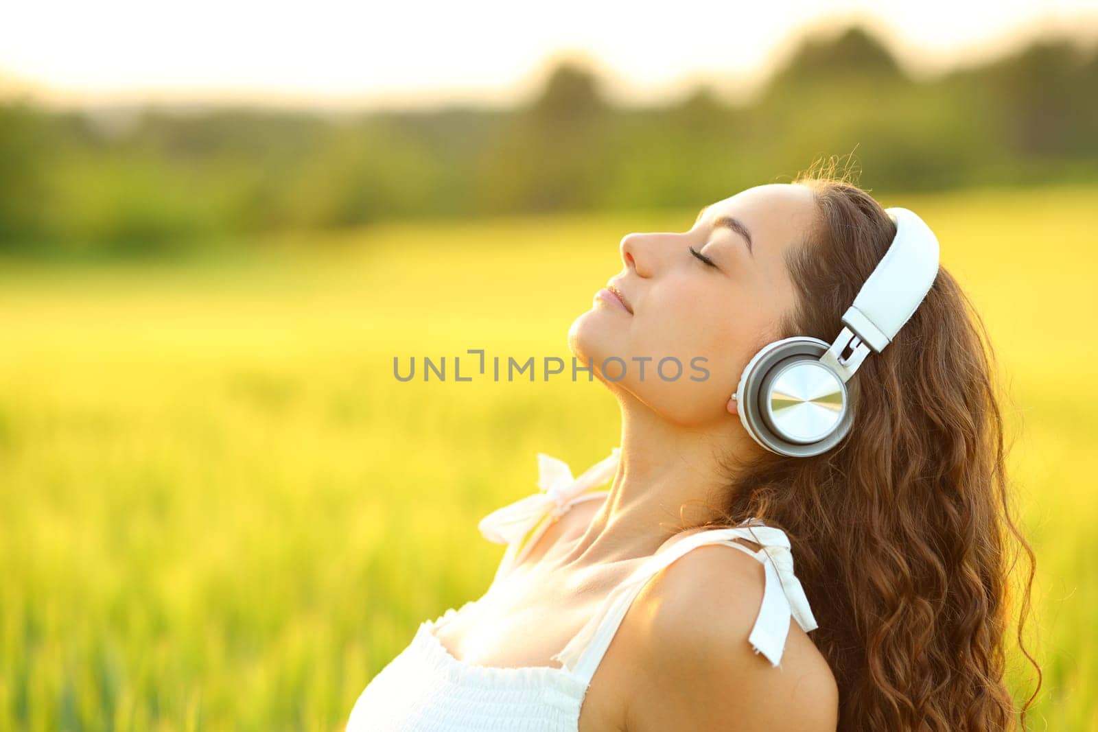 Side view portrait of a woman meditating listening music with headphones in a wheat field
