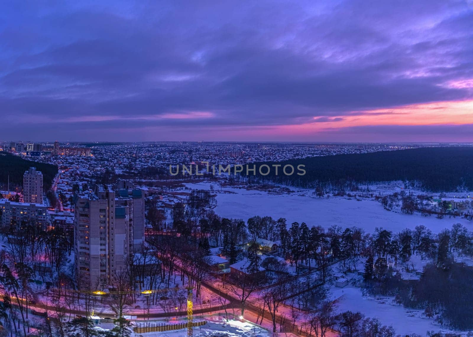 Sunset over the outskirts of the city of Kyiv and snow-covered forest in winter. Kyiv, Ukraine