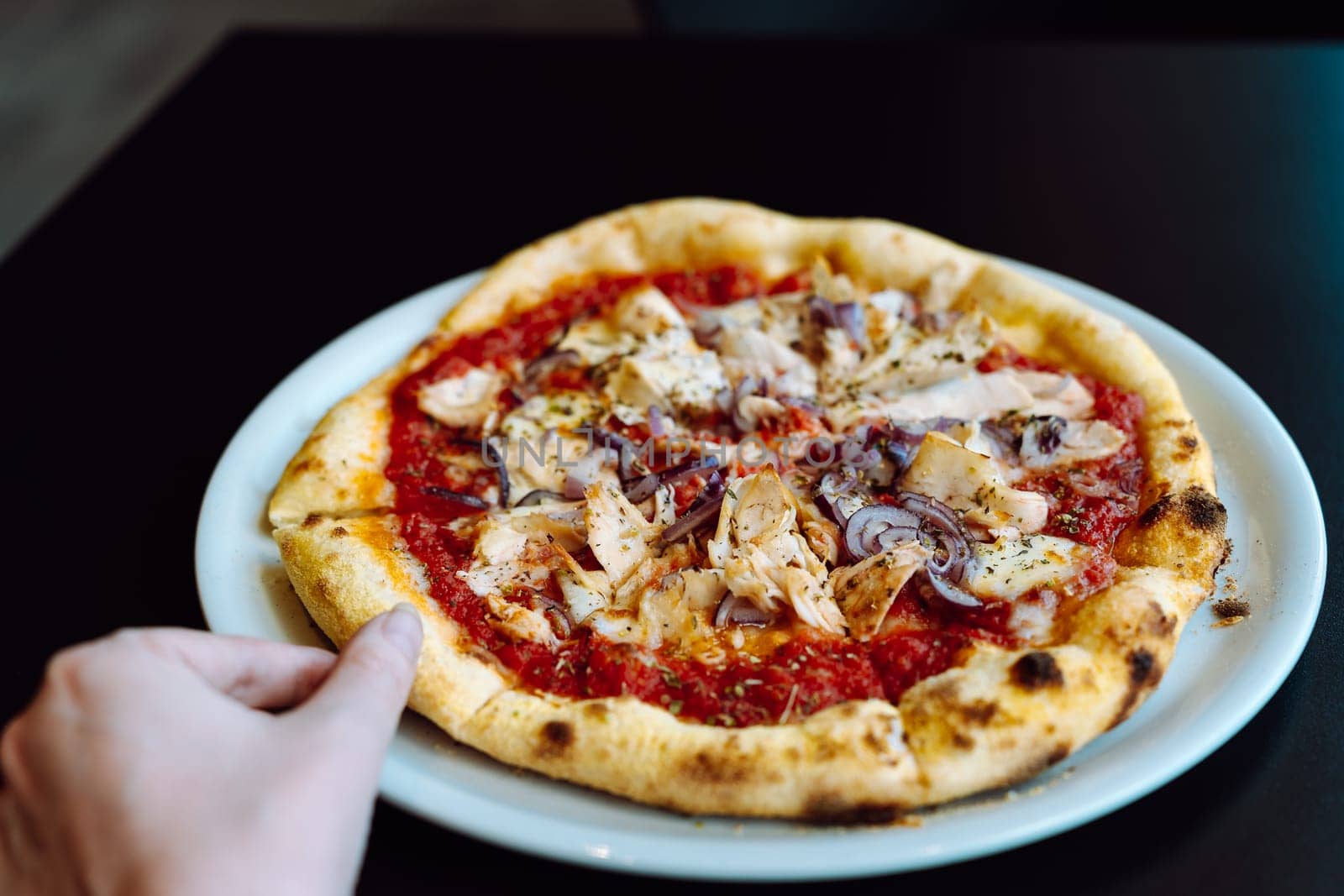 Hand takes a slice of pizza with chicken from a plate.