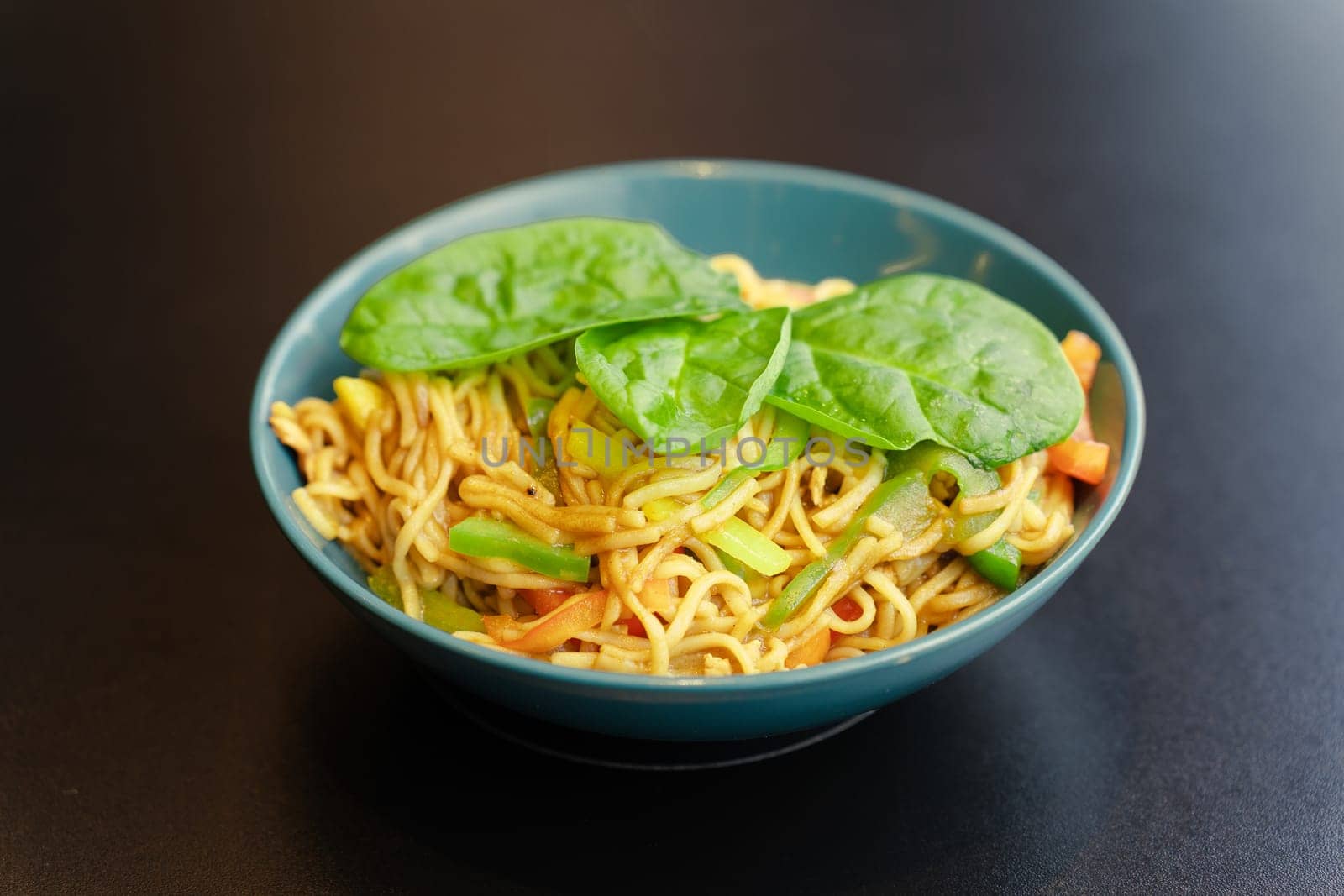 Spaghetti with vegetables and basil leaves in a turquoise plate, a kind of closeness