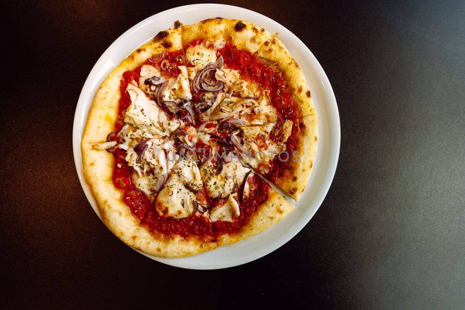 Top view of a pizza with chicken and red onions on a plate on a black table.