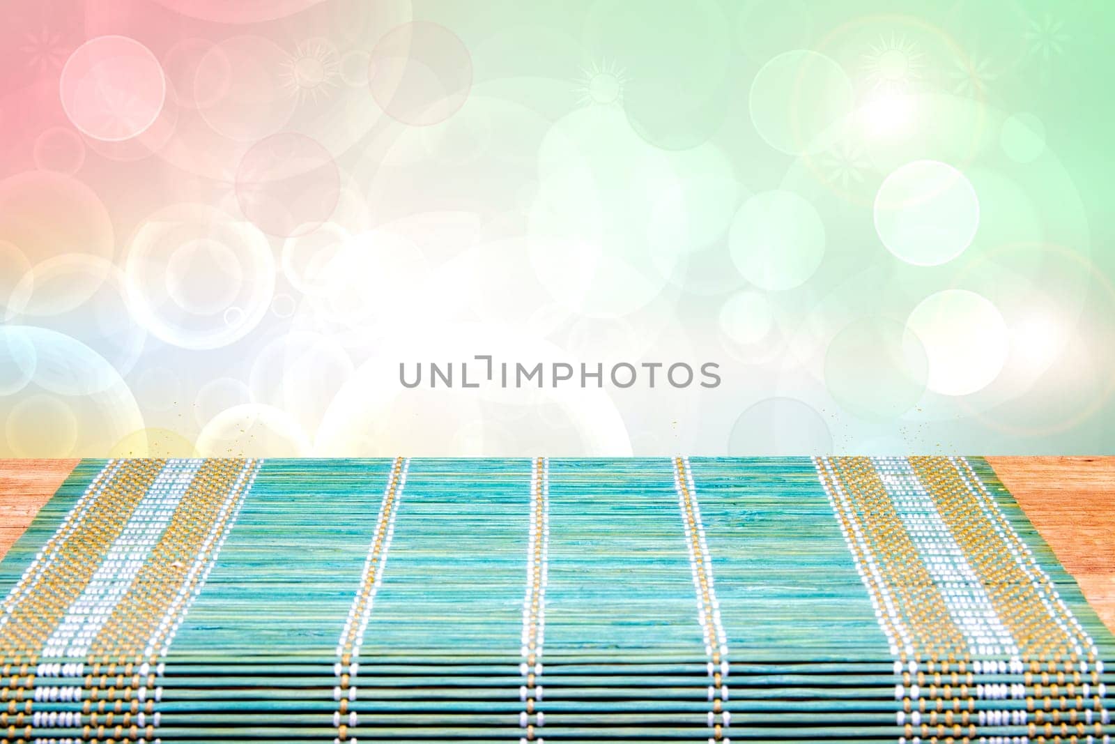 A green yellow bamboo mat on a rustic wooden table over bright blurred abstract background. Template for your product display montage. Space for design.