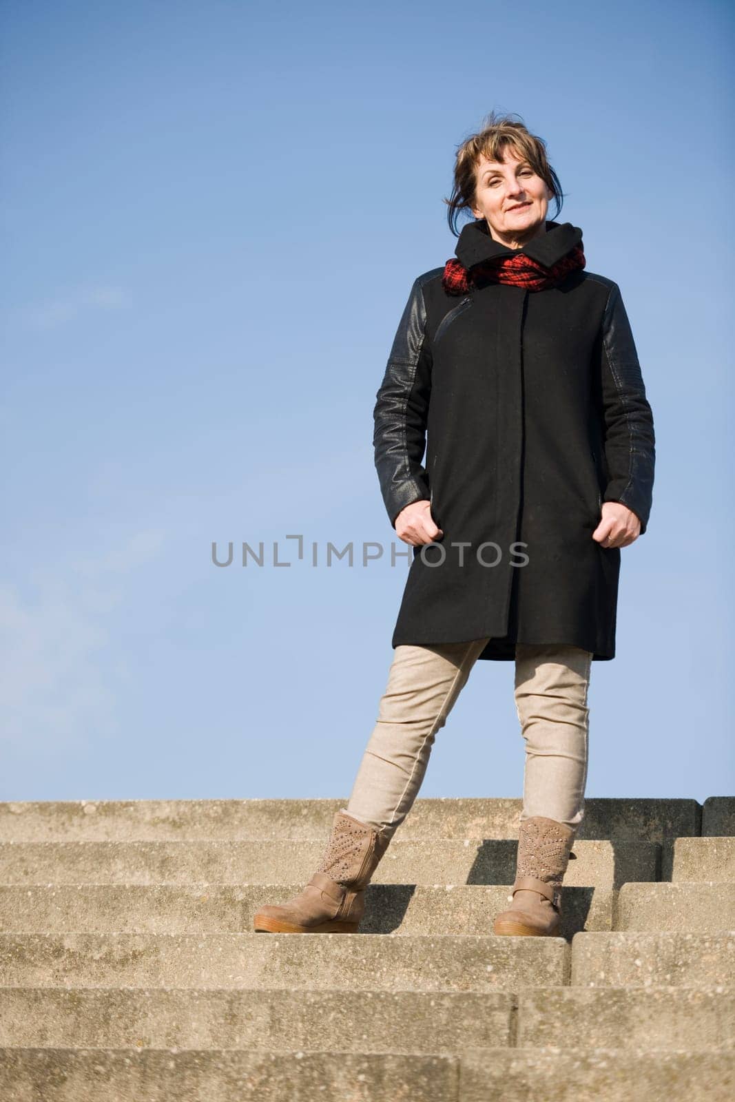 frontal full-body portrait of a mature woman in black leather jacket standing on a staircase in undersight