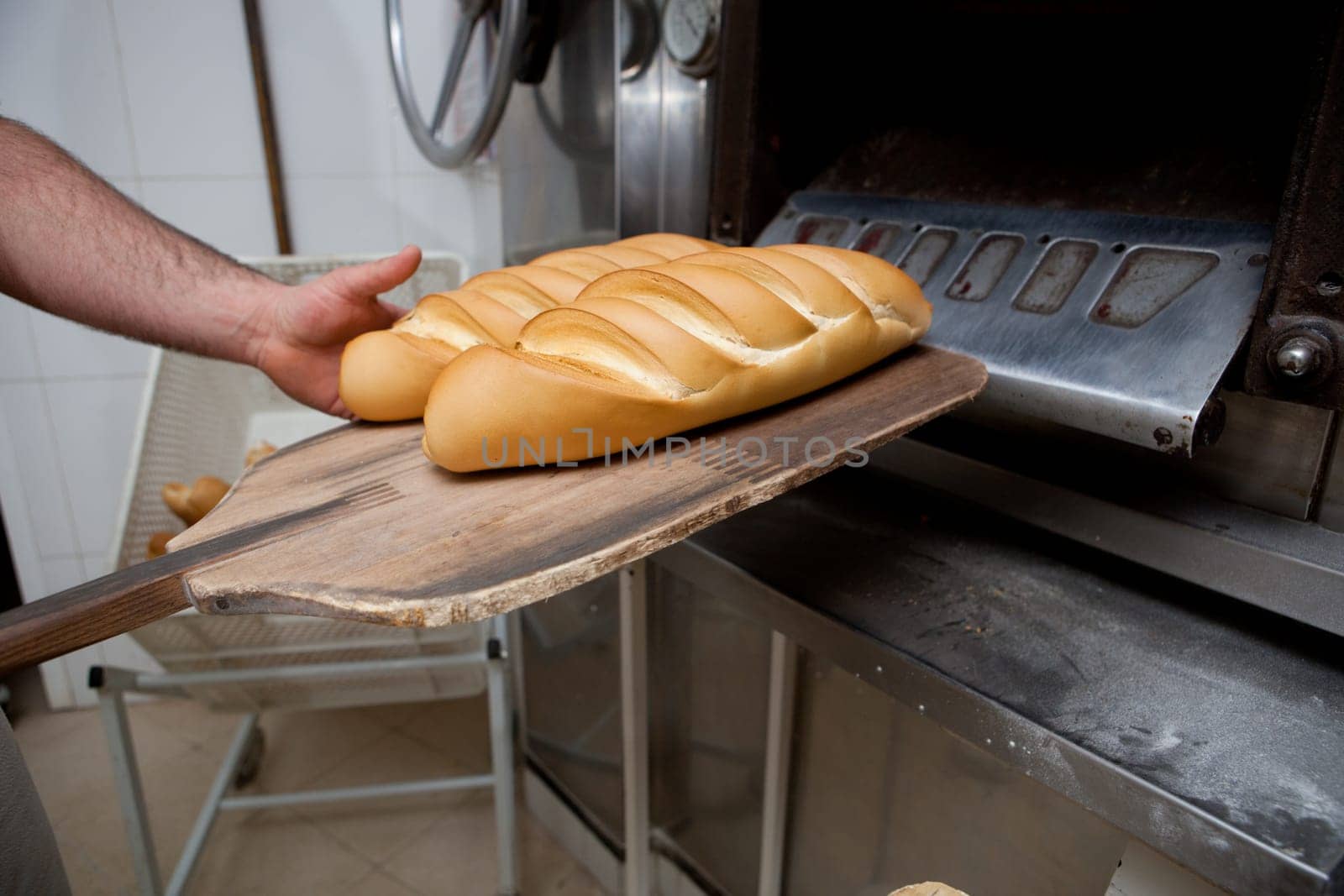 Baker taking fresh baked bread from oven. Manufacturing process of spanish bread