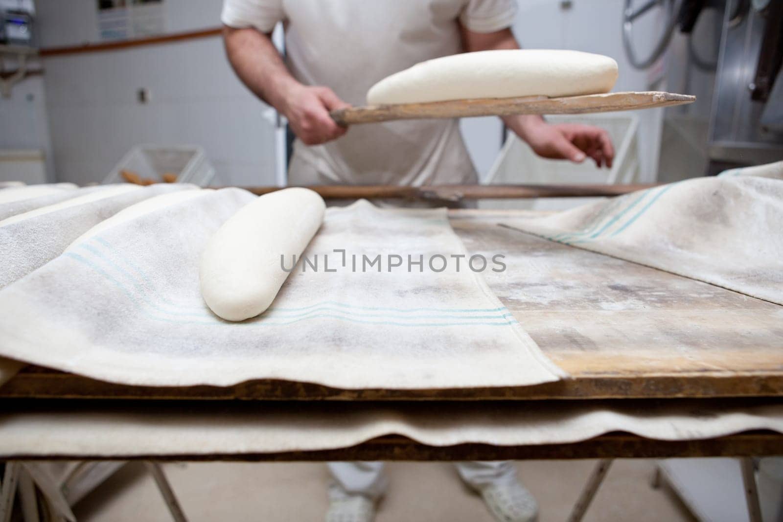 Baker holding the oven slice with raw bread. Manufacturing process of spanish bread