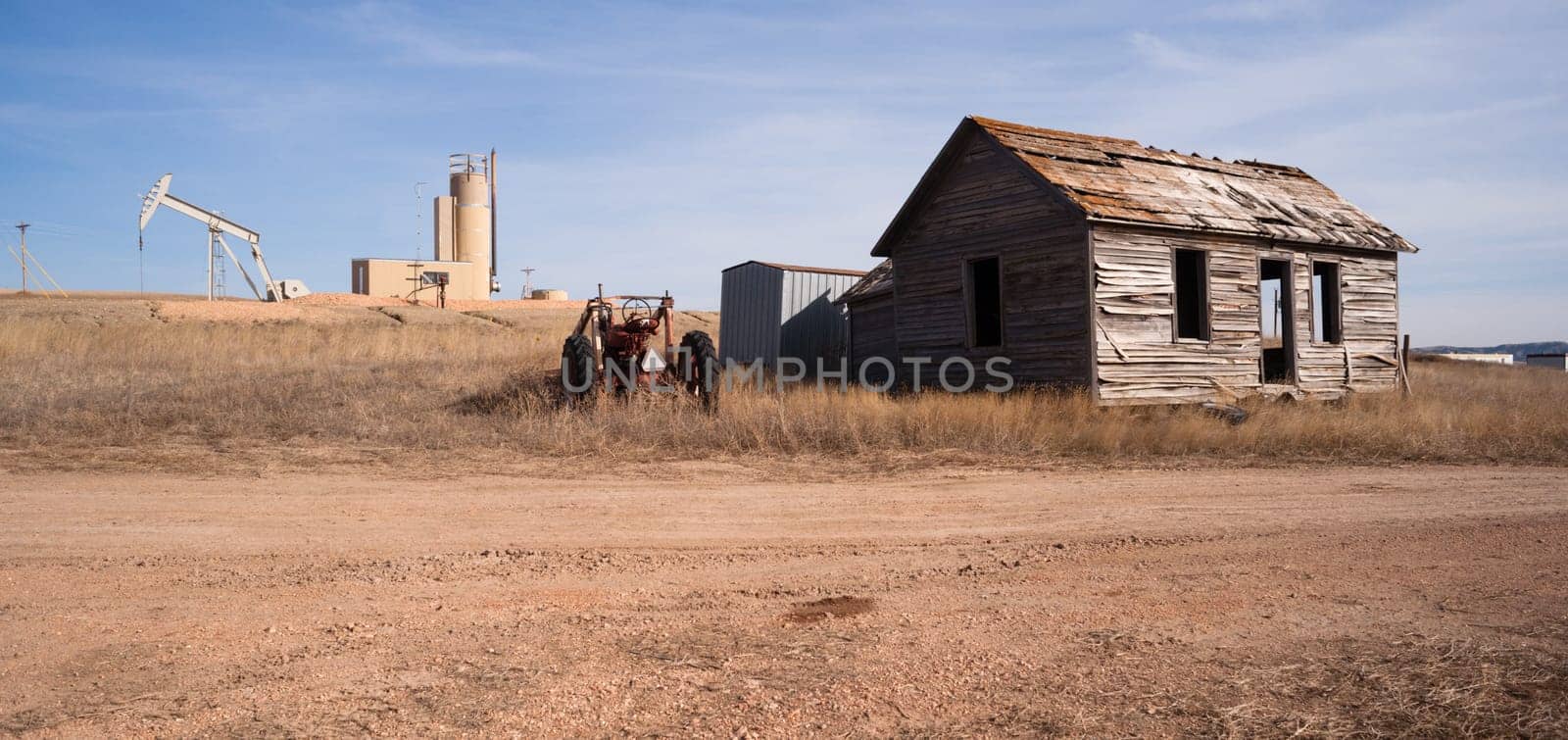 An abandoned tractor and cabin sit in the foreground of a fracking oil pump jack