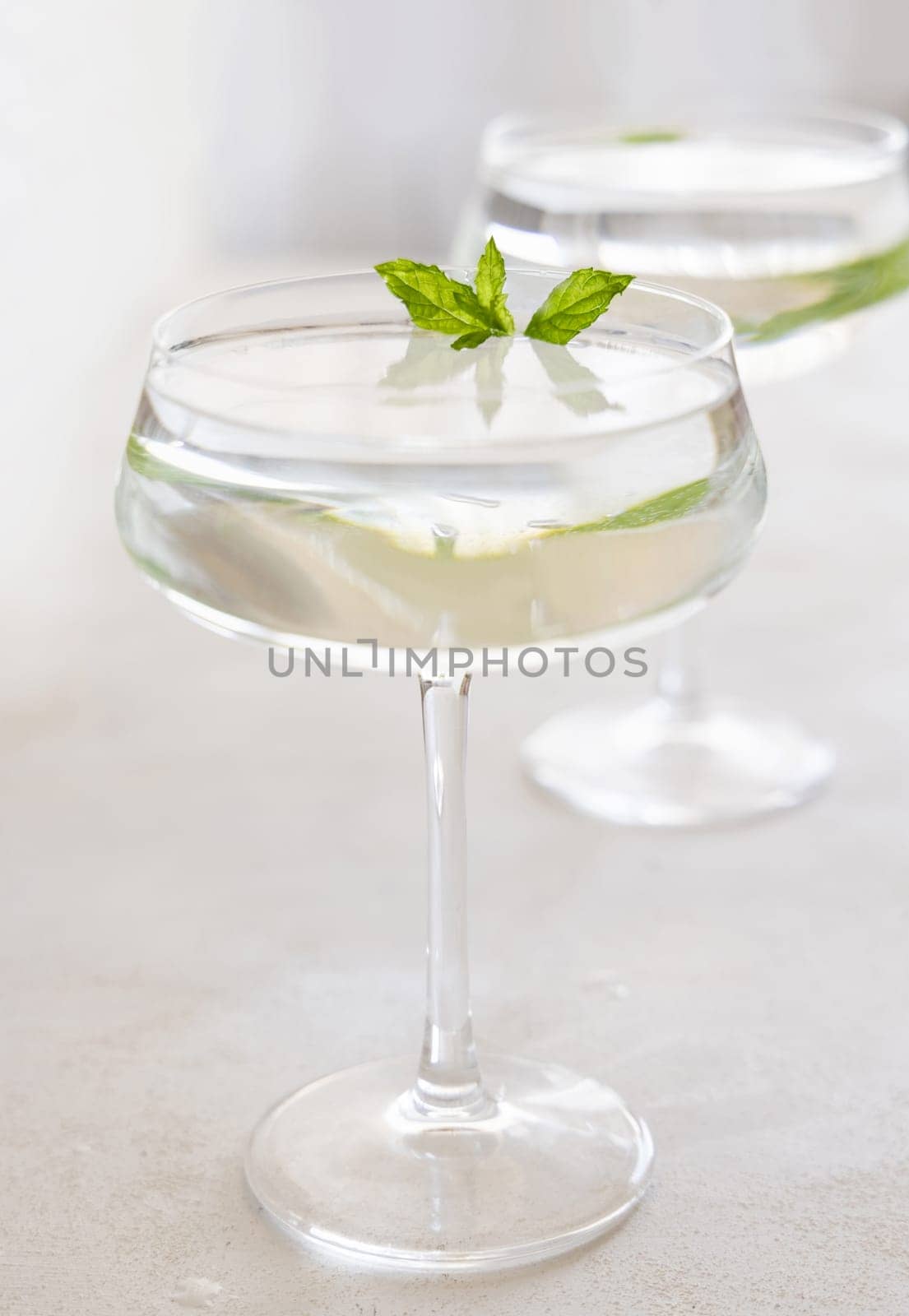 Transparent cocktail with ice cubes in a glass decorated with mint leaves close up. Tropical drink at the bar. Summer vacation mood. Analcolic mocktail drink
