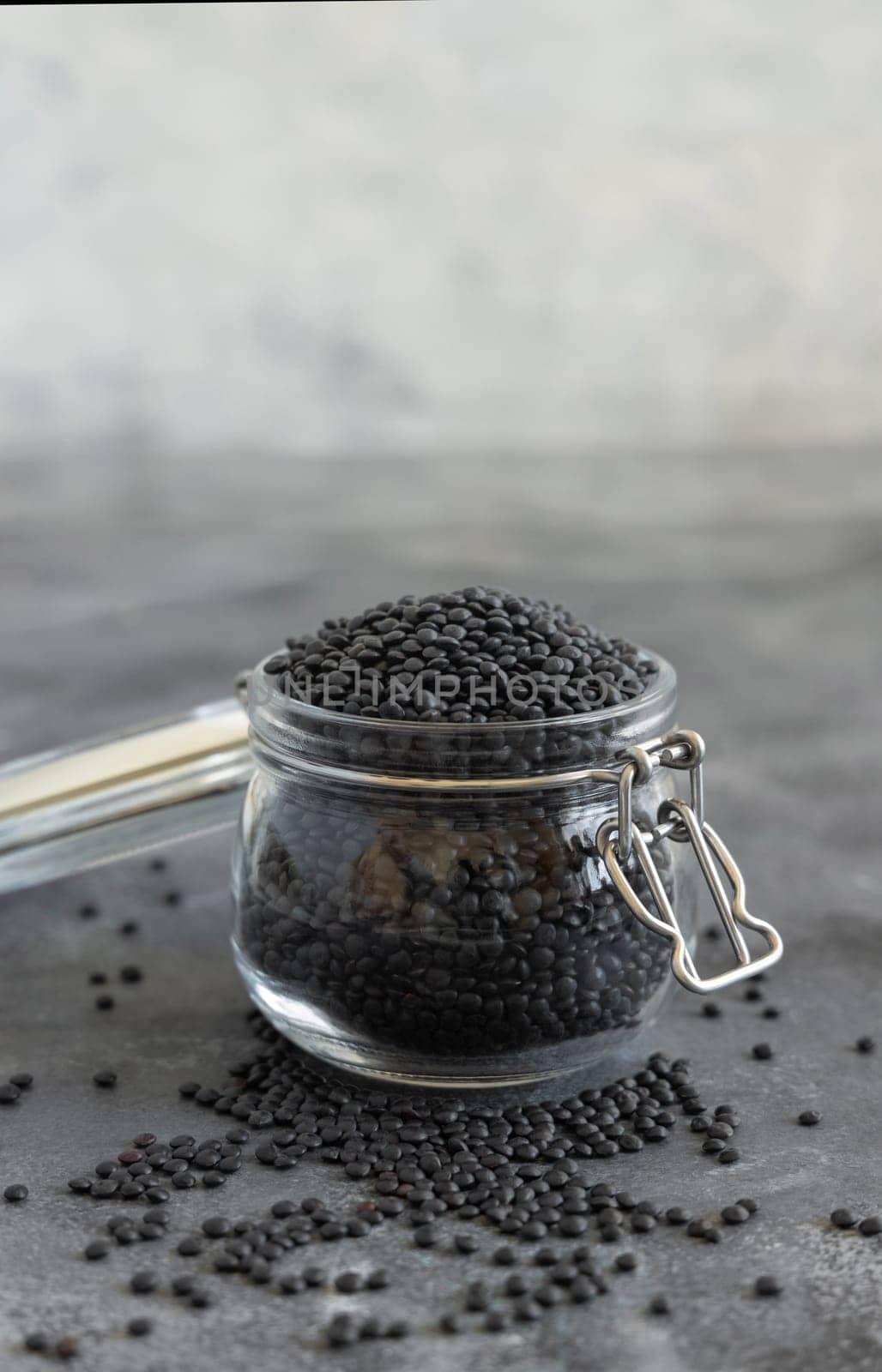 Glass jar of dry black lentils beans on grey table close up. Healthy eating, protein source for vegan and vegetarian diet. Traditional Asian and North African cuisines ingredient